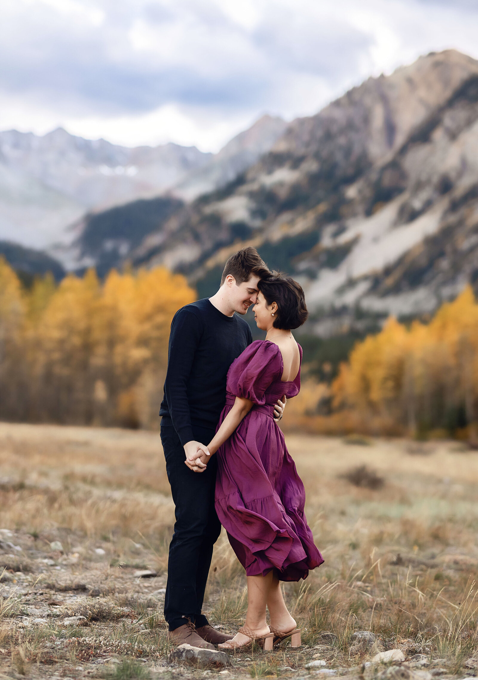 A young woman and young man hold hands and embrace during their engagement photoshoot in Aspen, Colorado,