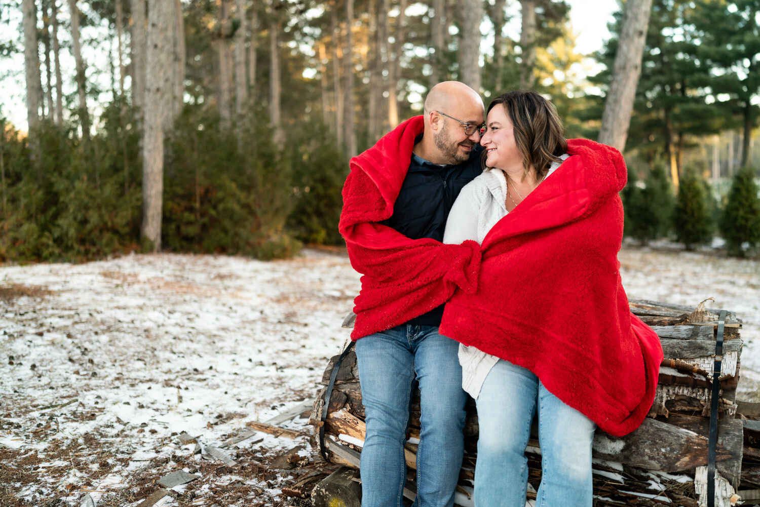 Mixed race couple snuggle in a red blanket in a snowy field.