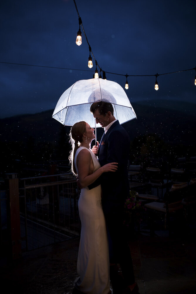 bride and groom standing in the rain under an umbrella