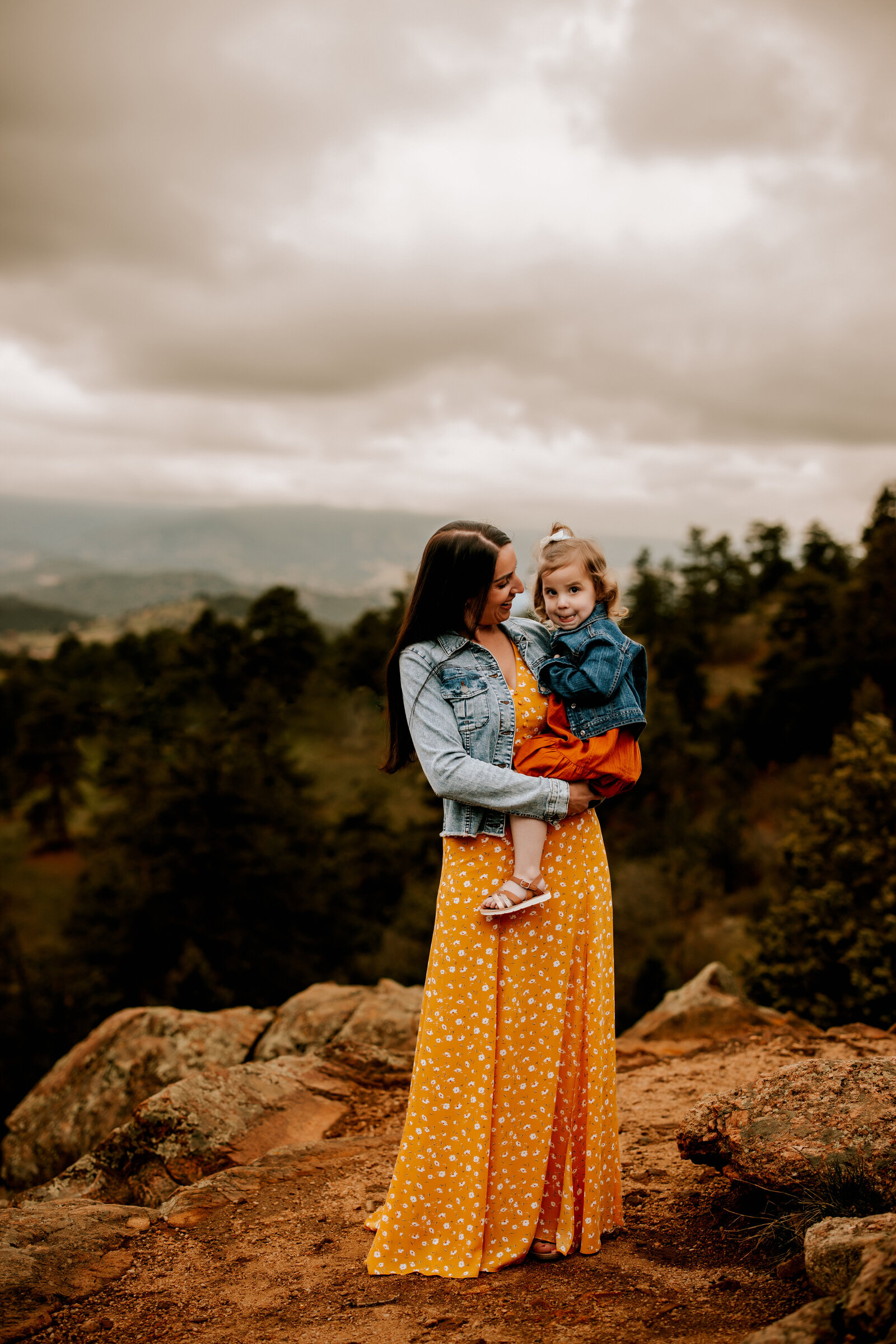 mom in yellow dress holsds toddler daughter on top of a mountain for family phots in denver colorado