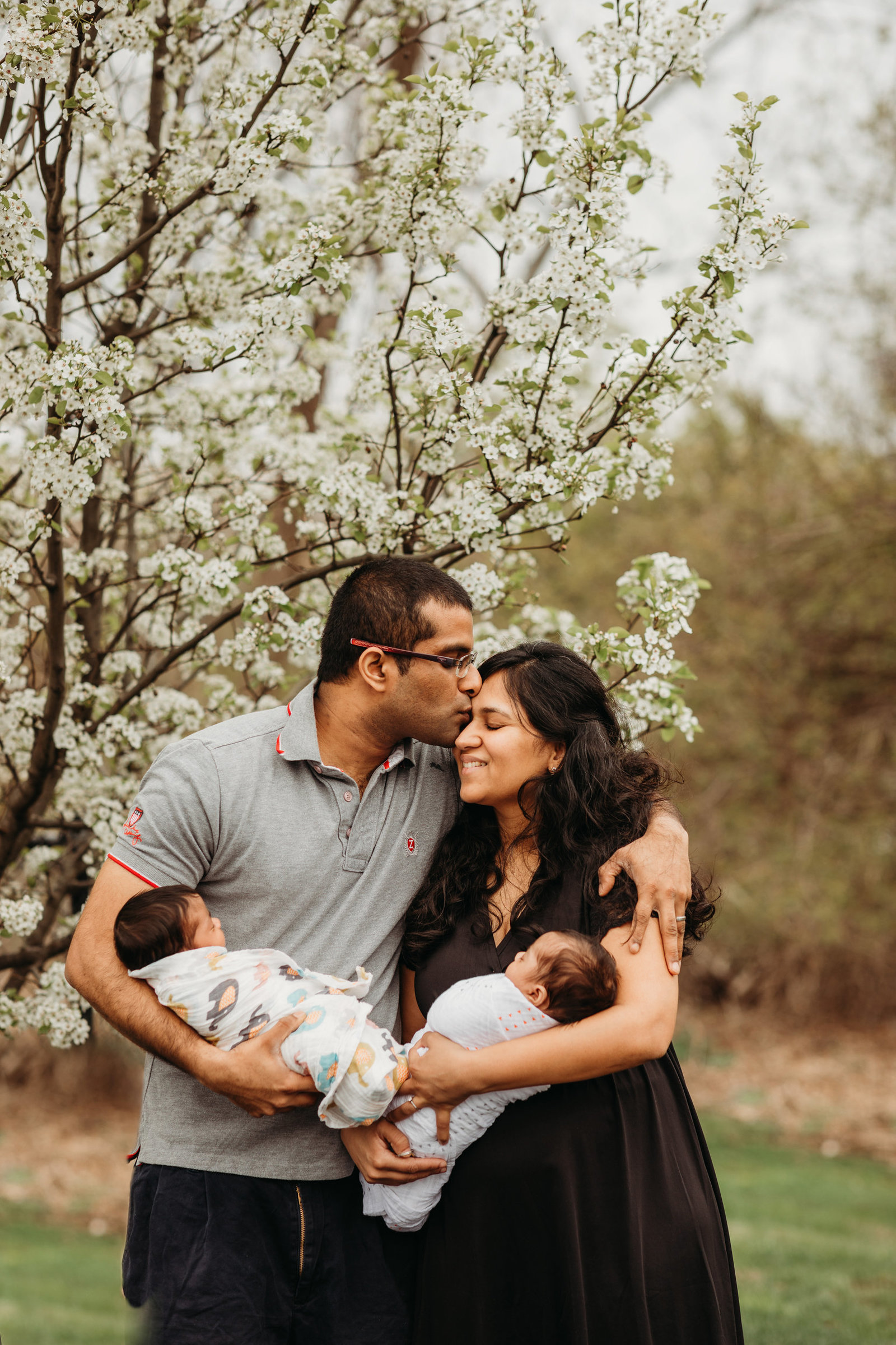 couple holding twins in front of a blossoming tree