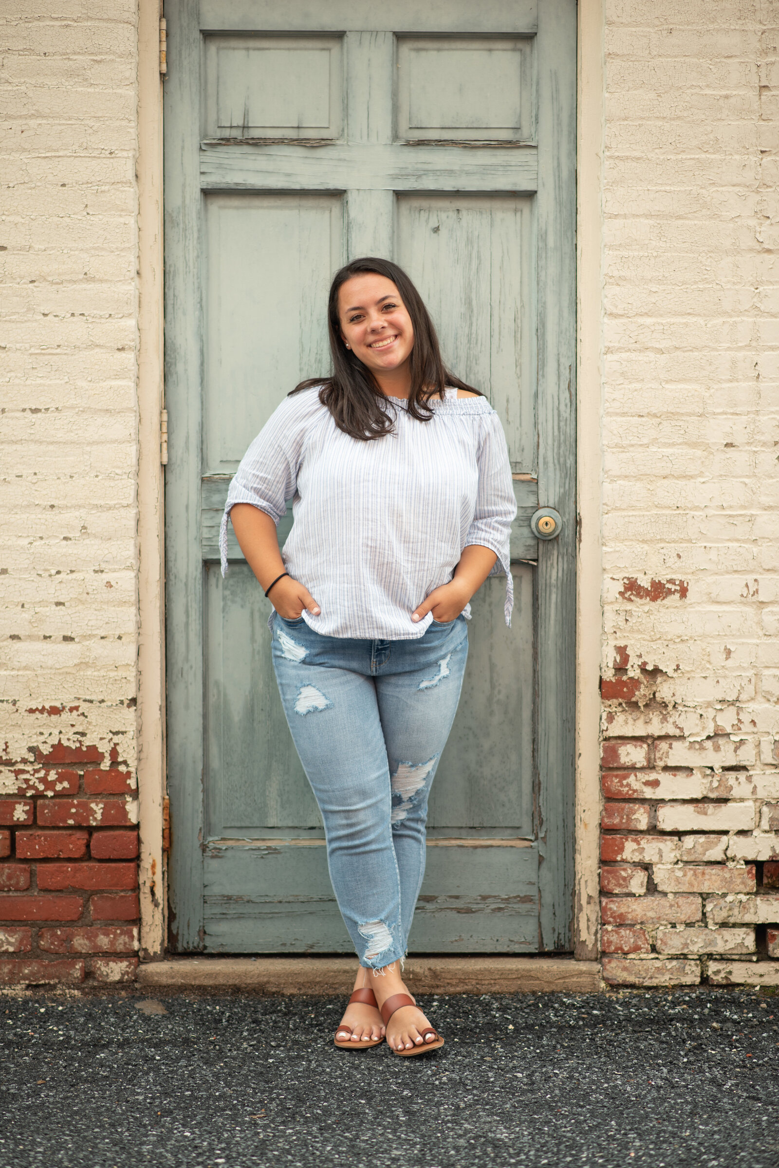 Senior girl in jeans in front of distressed door and brick wall