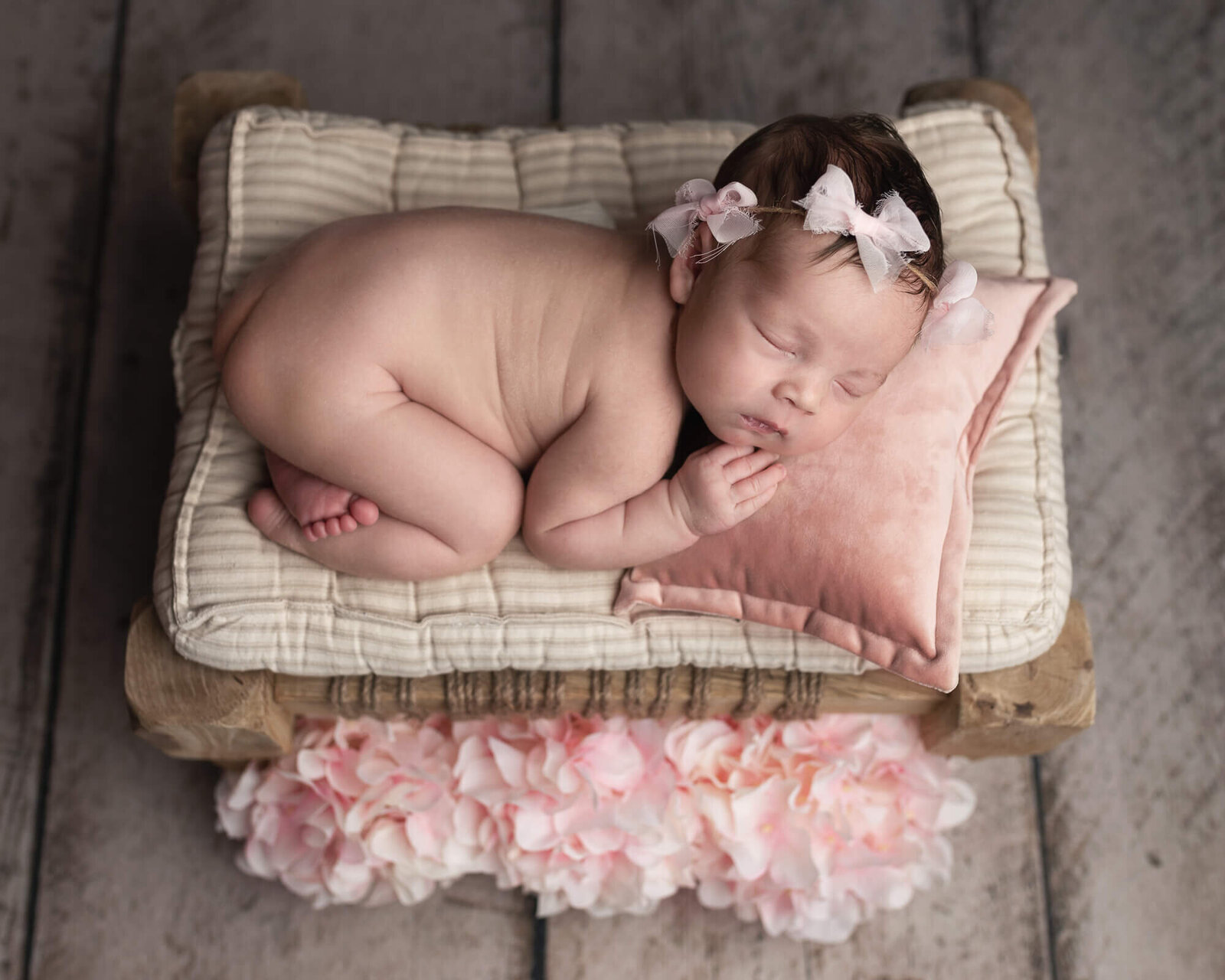 newborn girl curled up on bed with pink flowers