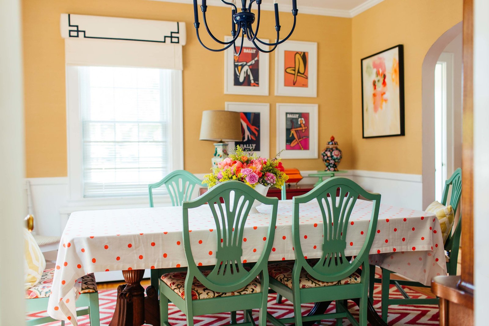 A yellow dining room with green chairs and chevron rug.