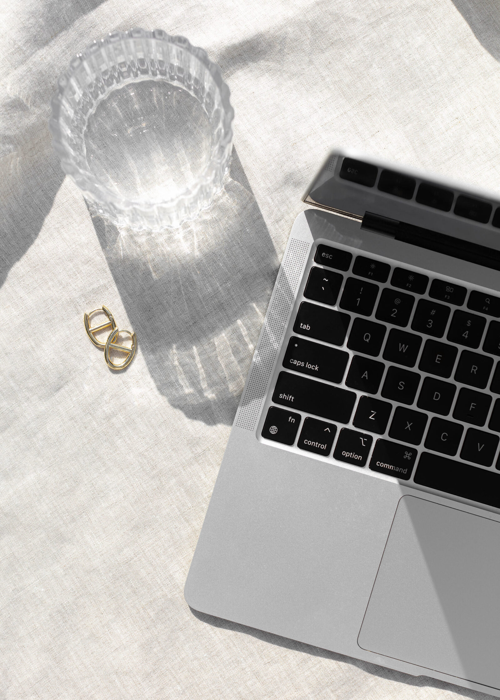 gold earrings next to a laptop with the shadow of a glass over it