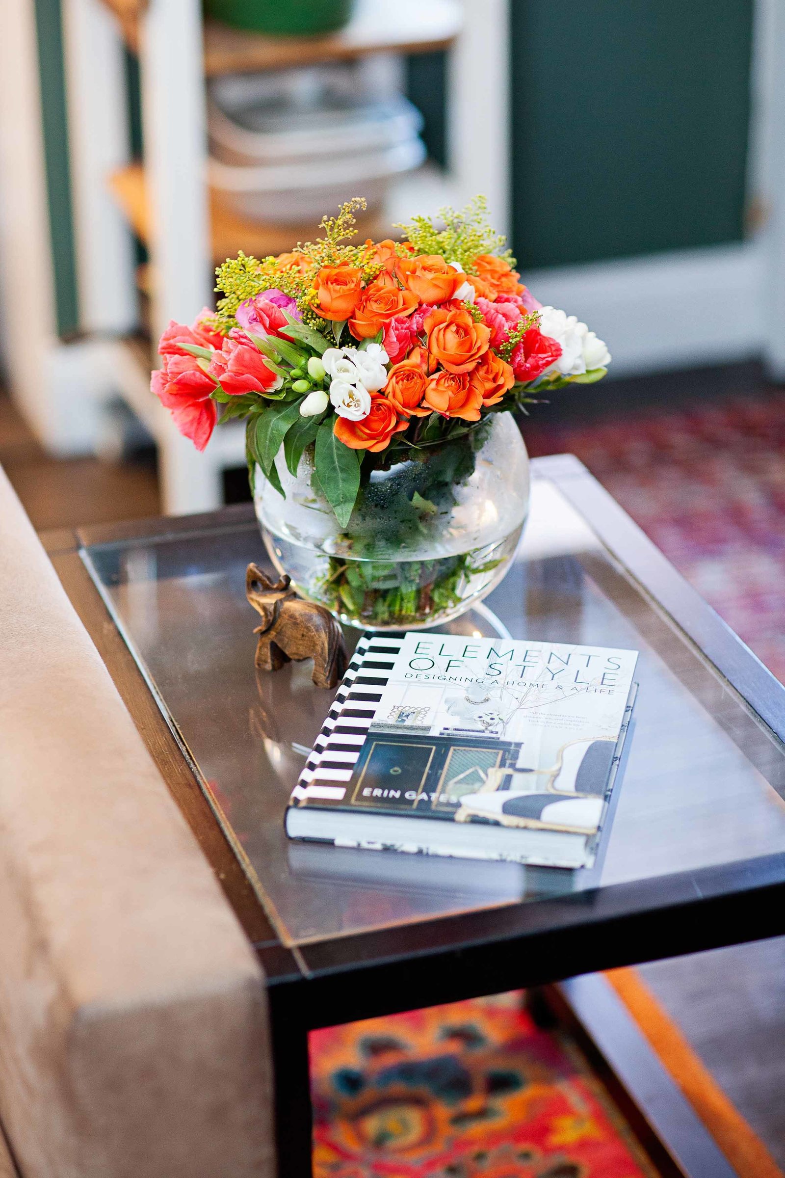 A glass end table with a book and fresh flowers.