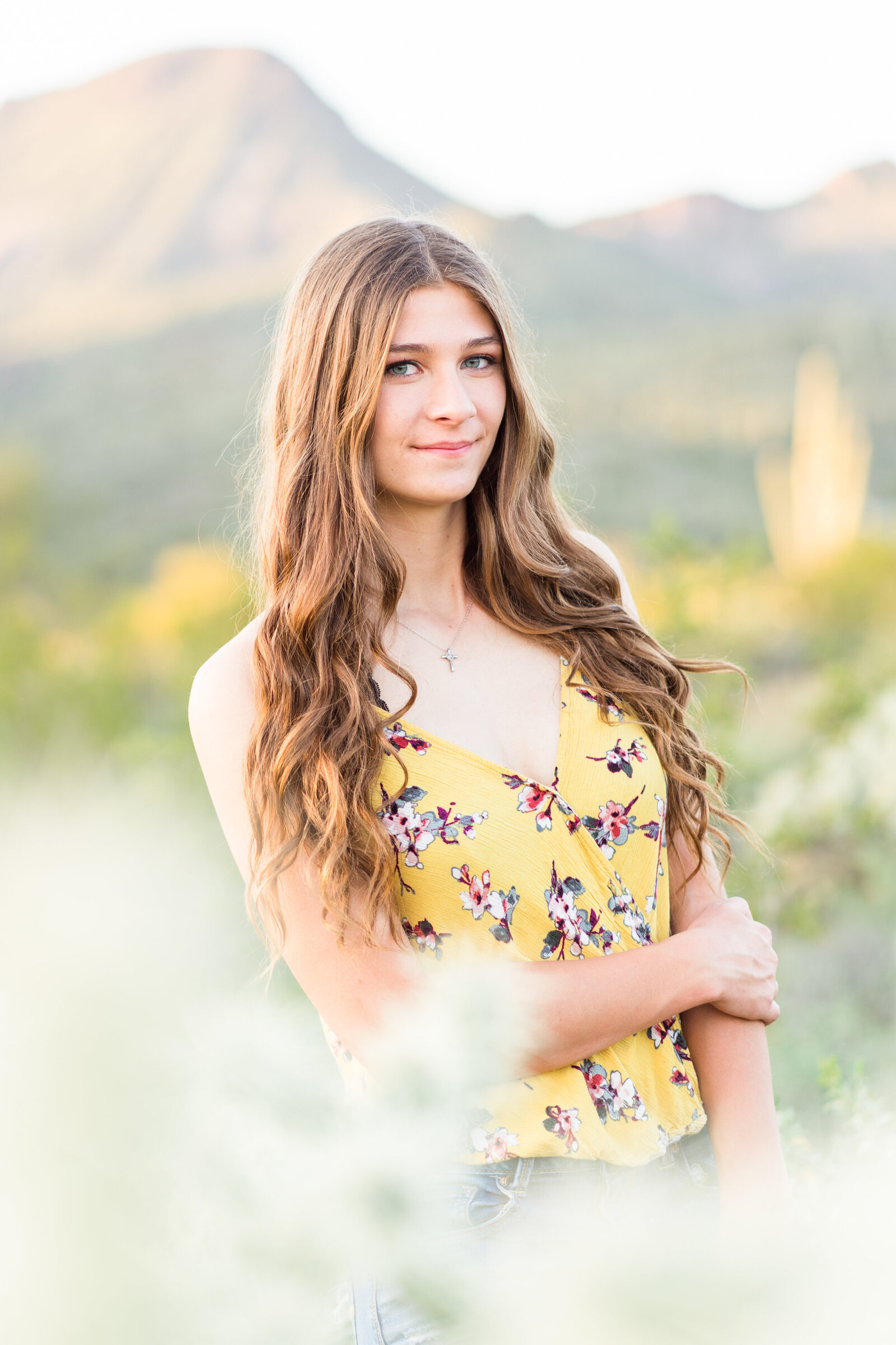 Senior girl smiling at camera wearing a yellow shirt in front of mountains in the desert