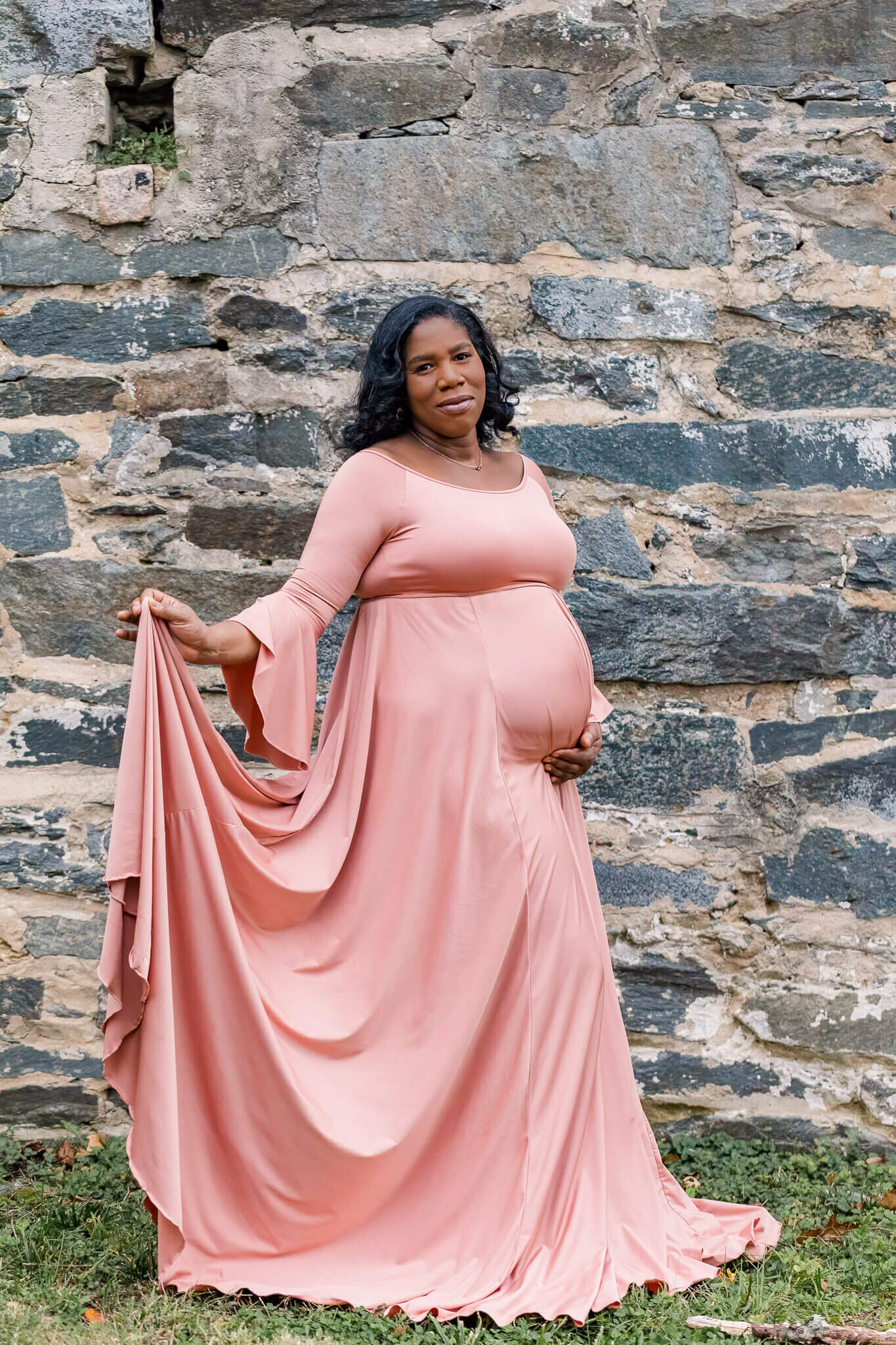 A pregnant woman in pink posing in front of a brick wall.