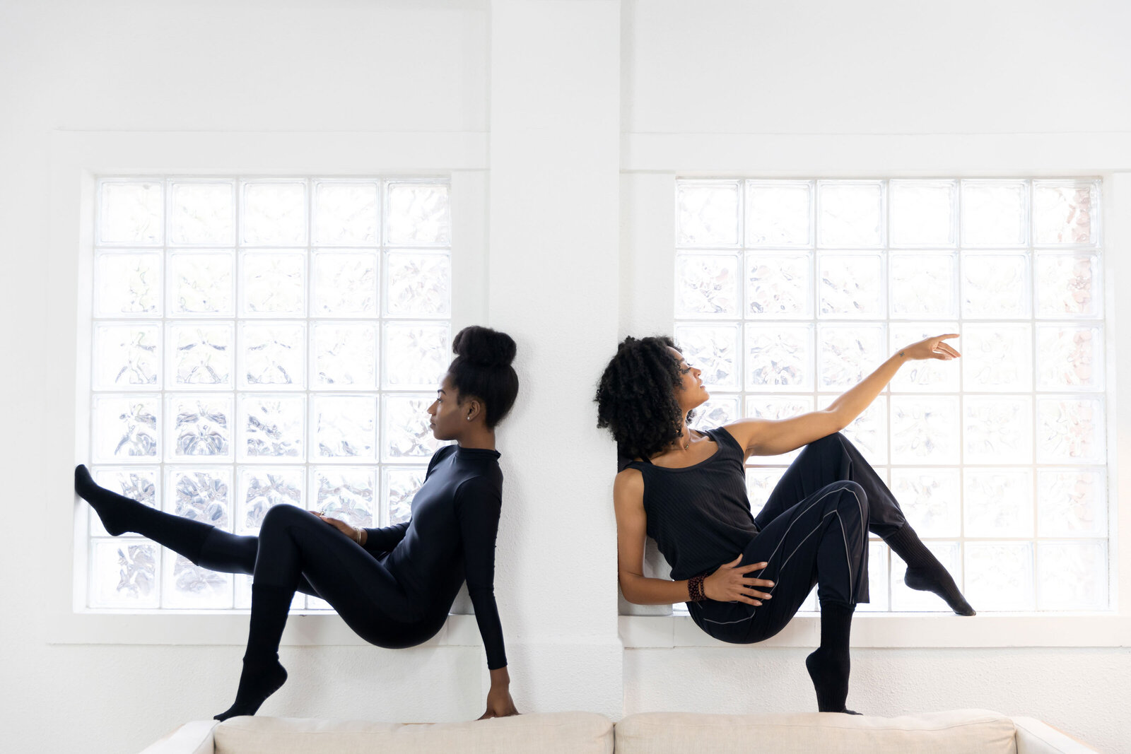 two seated Black women dancers with natural hair wearing black posing in windows