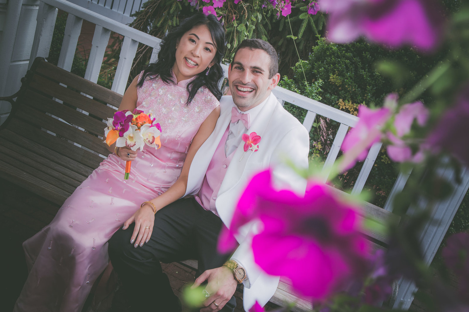 Couple looks at photographer and is framed in pink flowers.