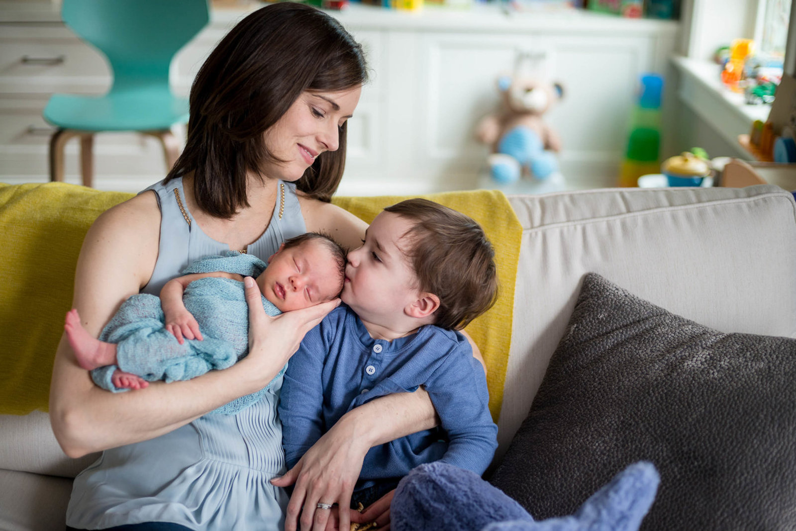 Brother kissing newborn head with mom holding baby at home lifestyle session