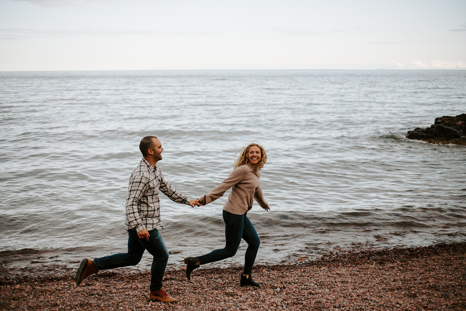 Couple holding hands running down the beach at the Noth Shore during their Minnesota engagement session