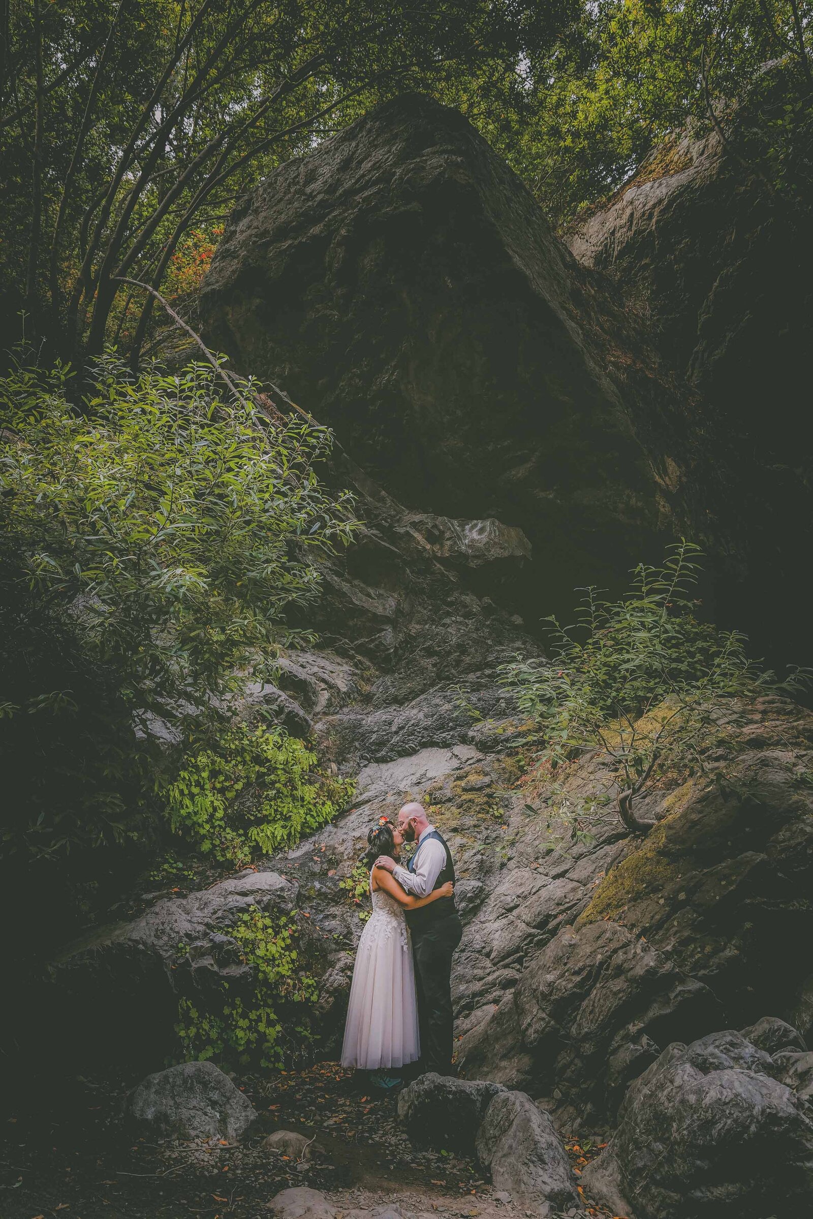 A bride wearing a flower crown kisses her groom in a forest setting in Cambria Big Sur.