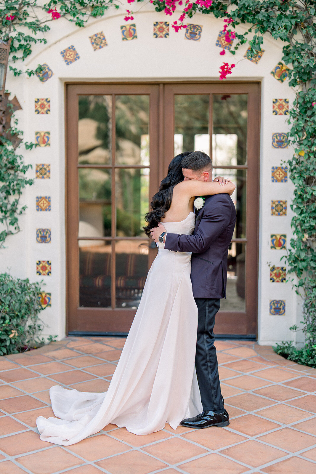 Bride and groom share a romantic embrace in front of Spanish-style doors adorned with climbing ivy and tile at Hummingbird Nest Ranch, captured in editorial film wedding photography.