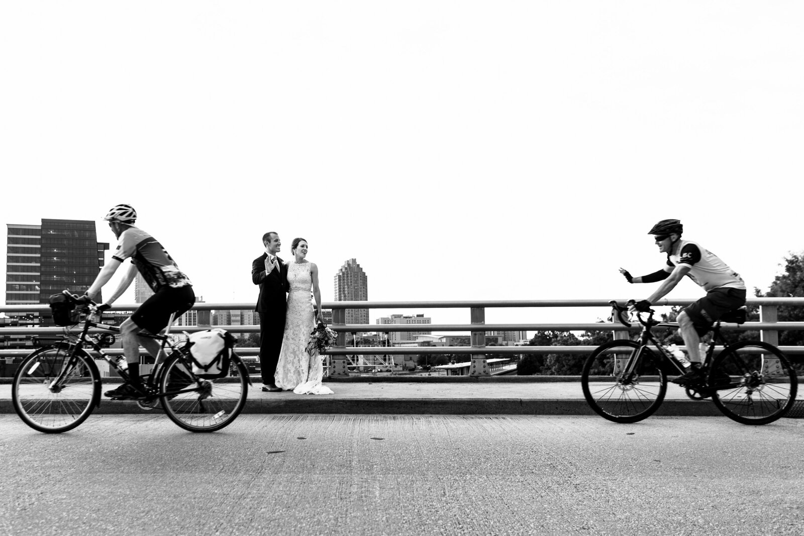 Newlywed couple stands on Boylan Bridge in Raleigh, NC as cyclists ride by