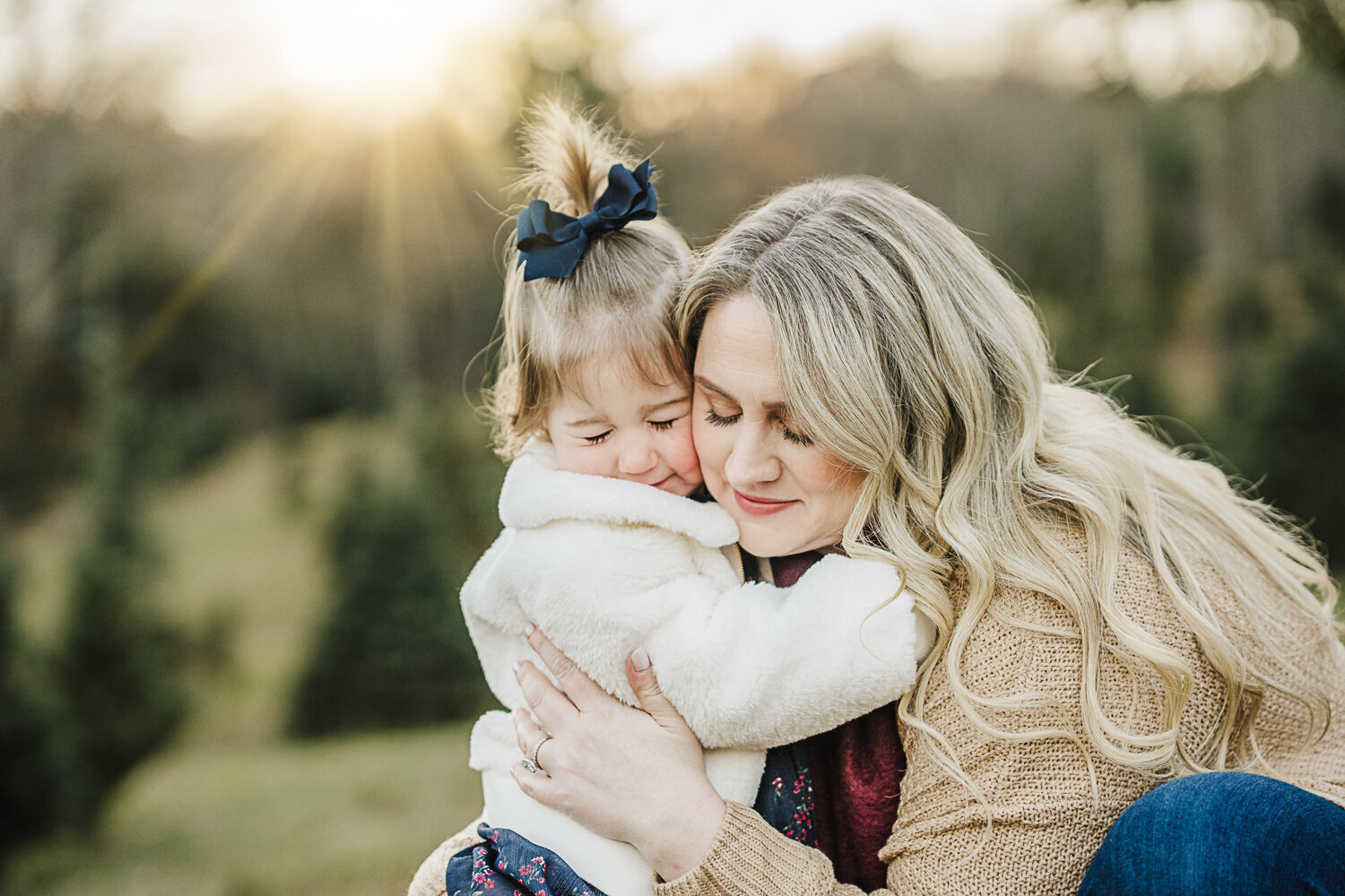 mom snuggles toddler girl at sunset in a tree farm