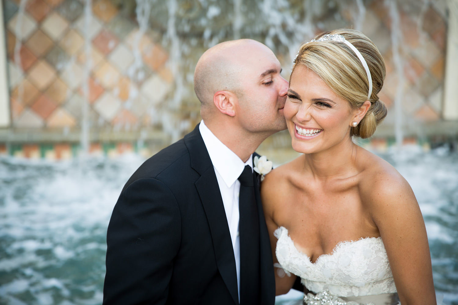Groom sneaks a kiss in front of the water fountain at St Regis Monarch Beach