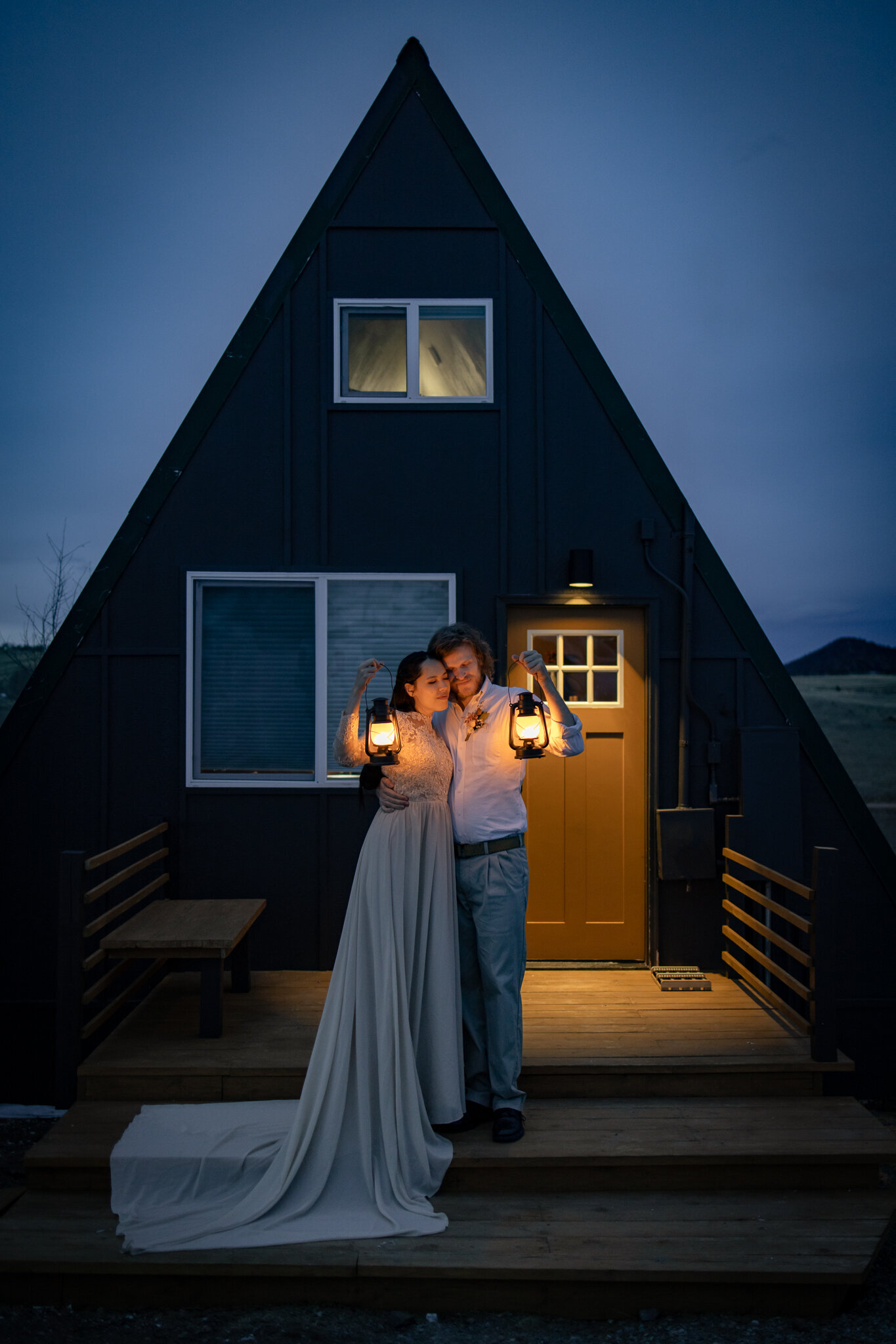 Bride and groom hold lanterns up in front of their A-Frame cabin during blue hour