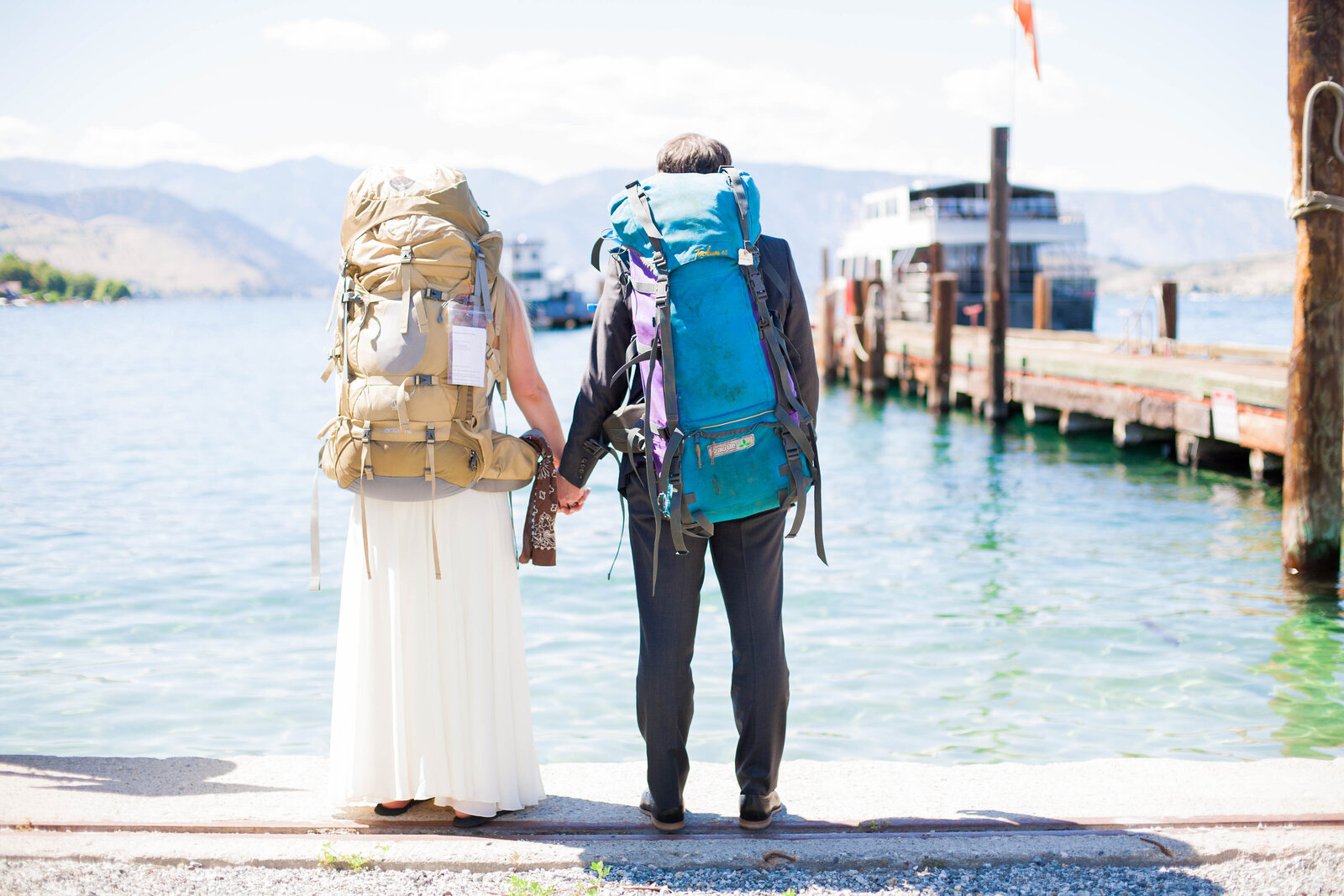 A bride wearing a wedding dress and a groom wearing a suit wearing backpacking gear.