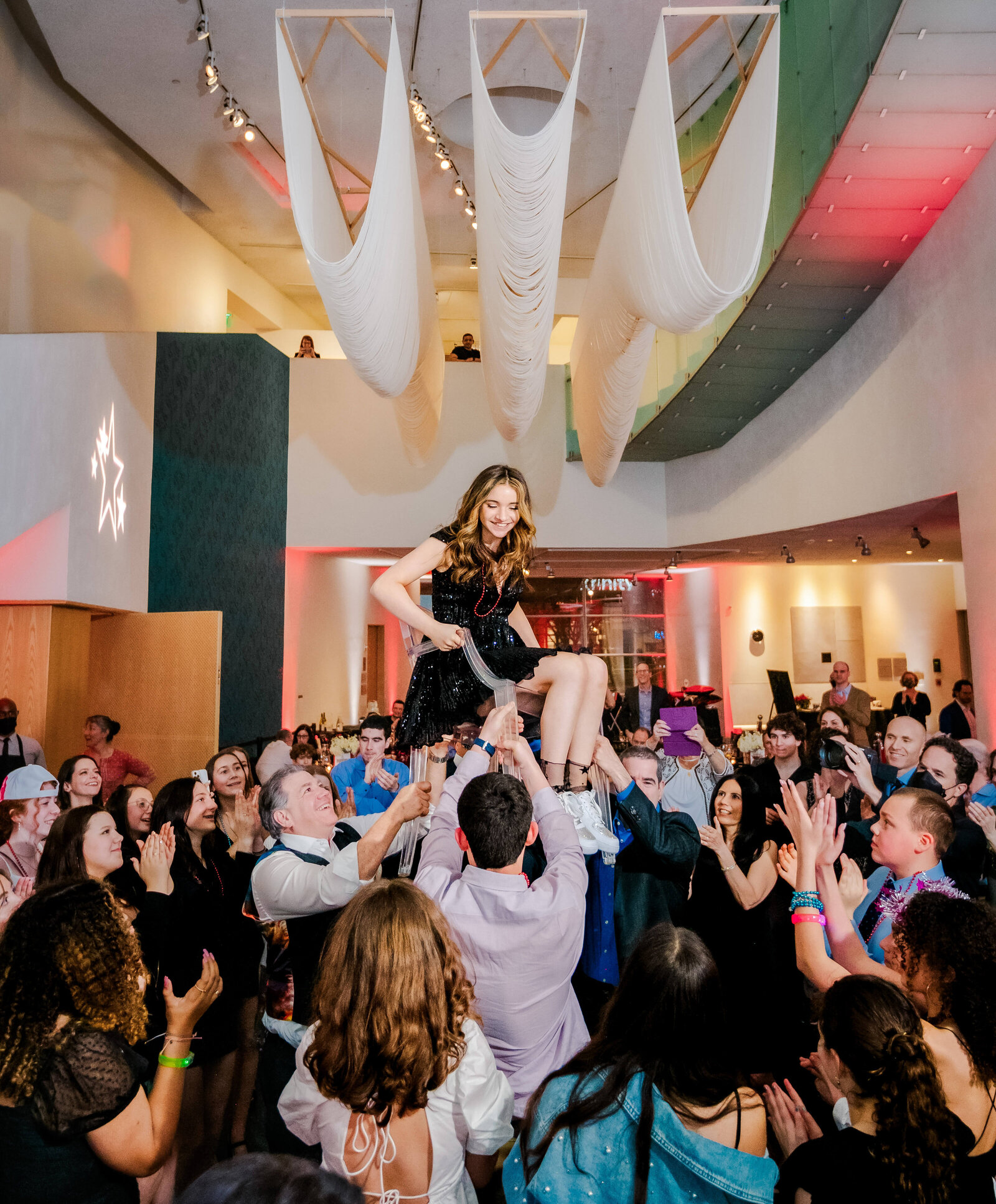 A Bellevue Bar and Bat Mitzvah Photography image of a crowded dance floor lifting the teen girl in a chair and celebrating