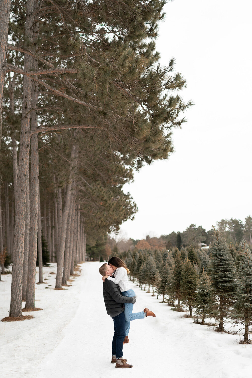 Man lifts and kisses woman in the snow at a Christmas tree lot in Anoka, Minnesota.