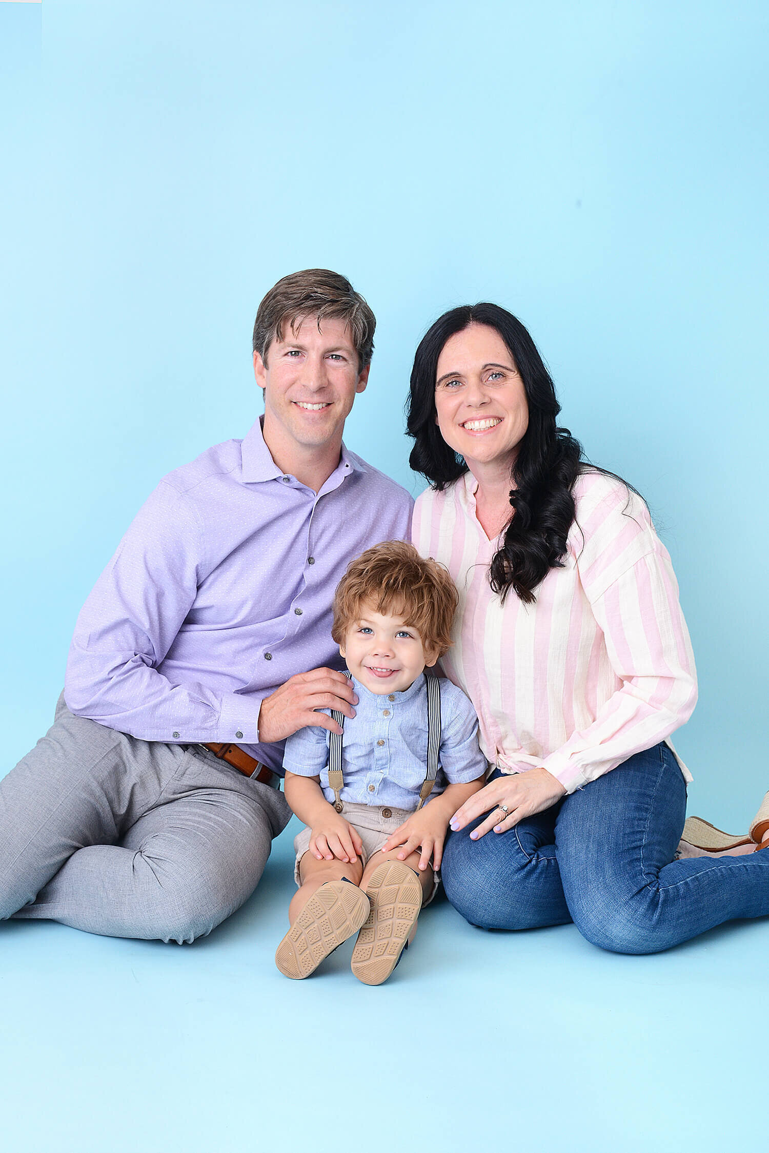 family smiles at their photography session in houston with a blue background