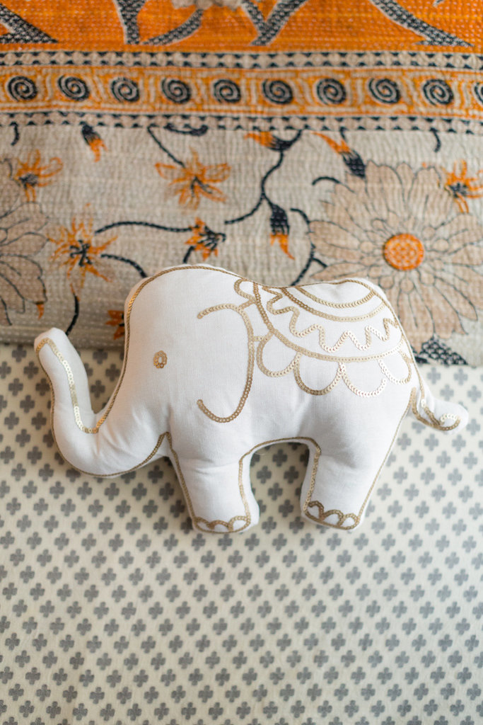 A white and gold stuffed elephant on a patterned duvet.