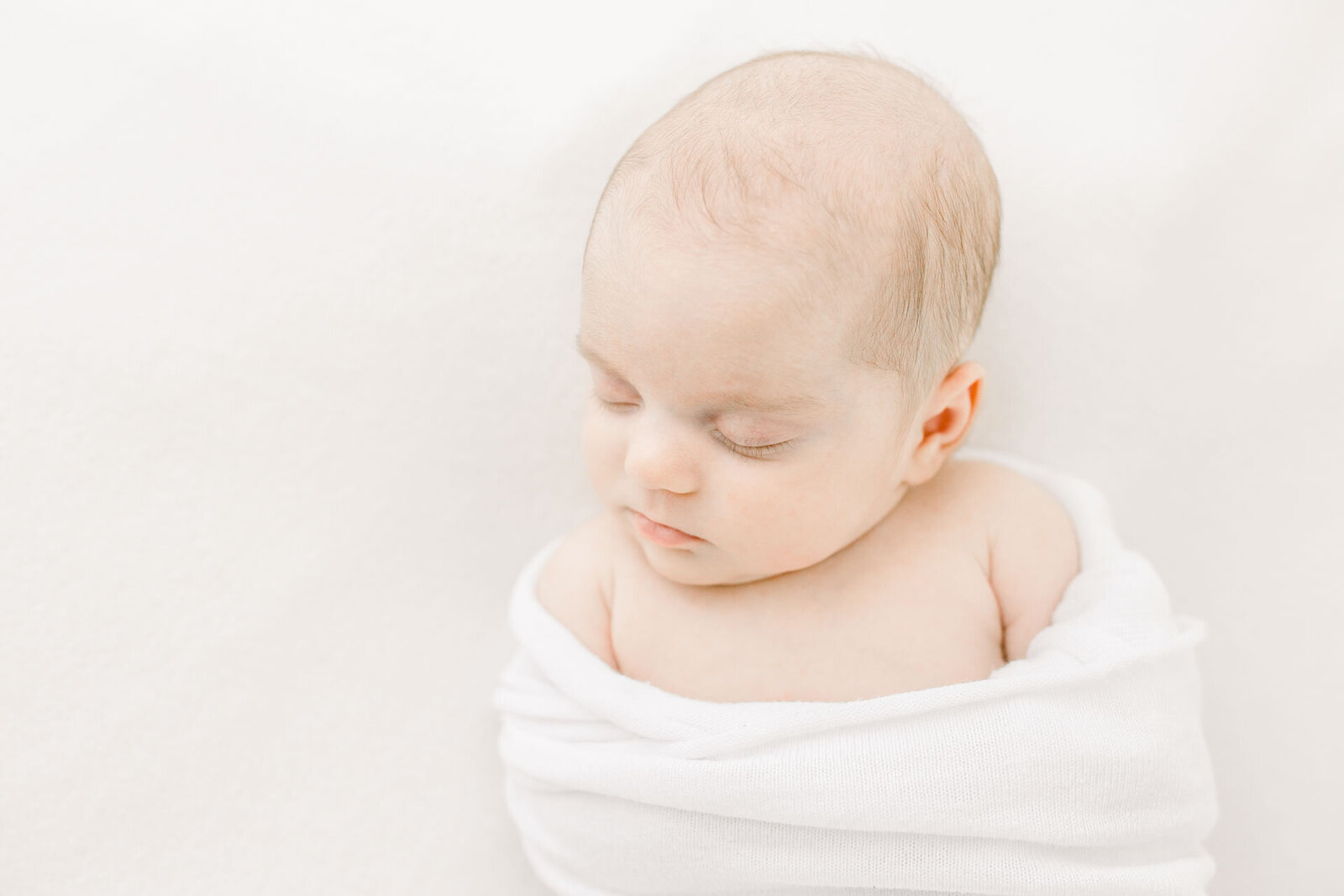 Zarte Neugeborenenfotografie mit Nahaufnahme eines schlafenden Babys. Alles in weiß.