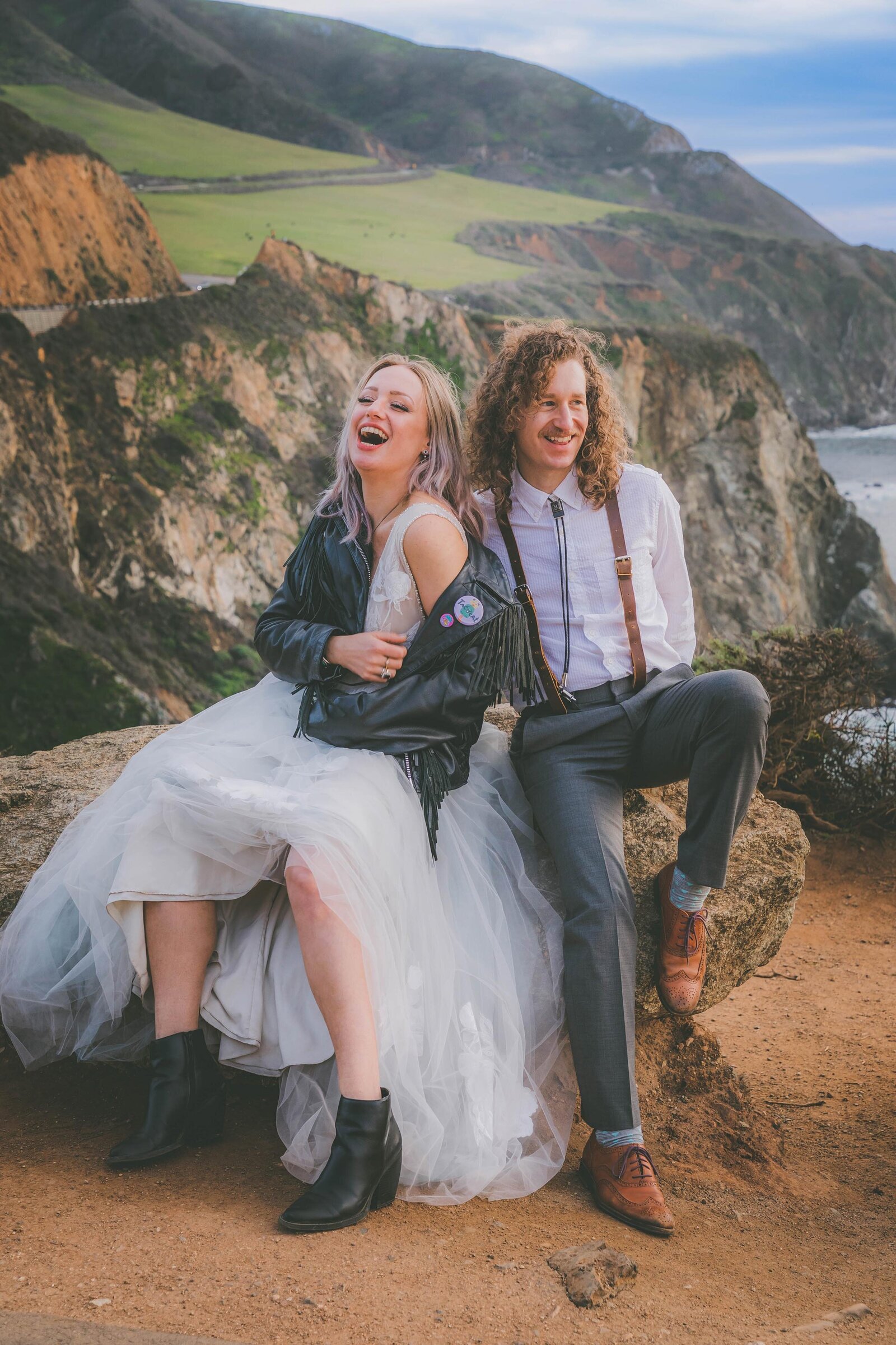 A bride and groom laugh hysterically while posing for wedding portraits at Bixby Bridge in Big Sur.
