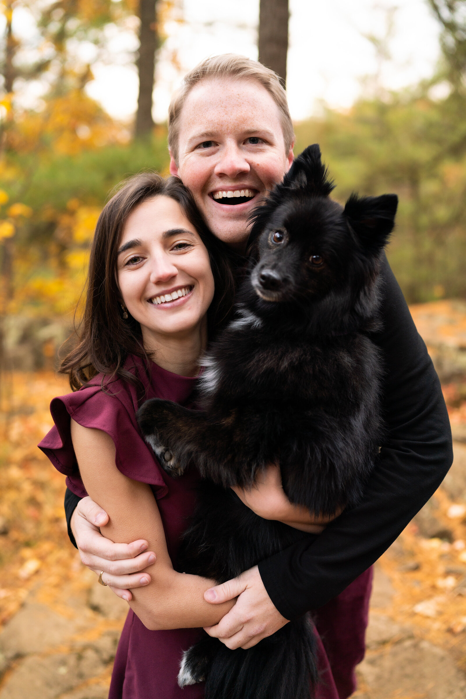 Man and woman smile while holding their black Pomeranian.