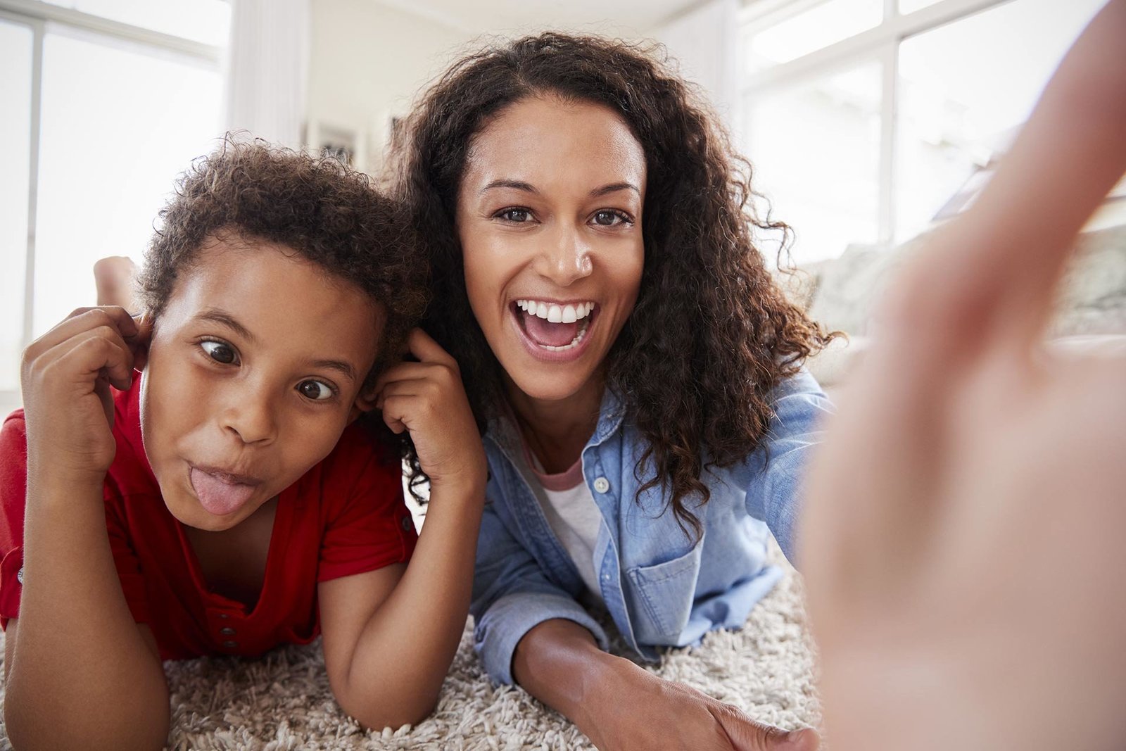 Playful Black mother and her preschool son making faces and enjoying playtime on the floor. Explore fun parenting activities with Successful Black Parenting Magazine.