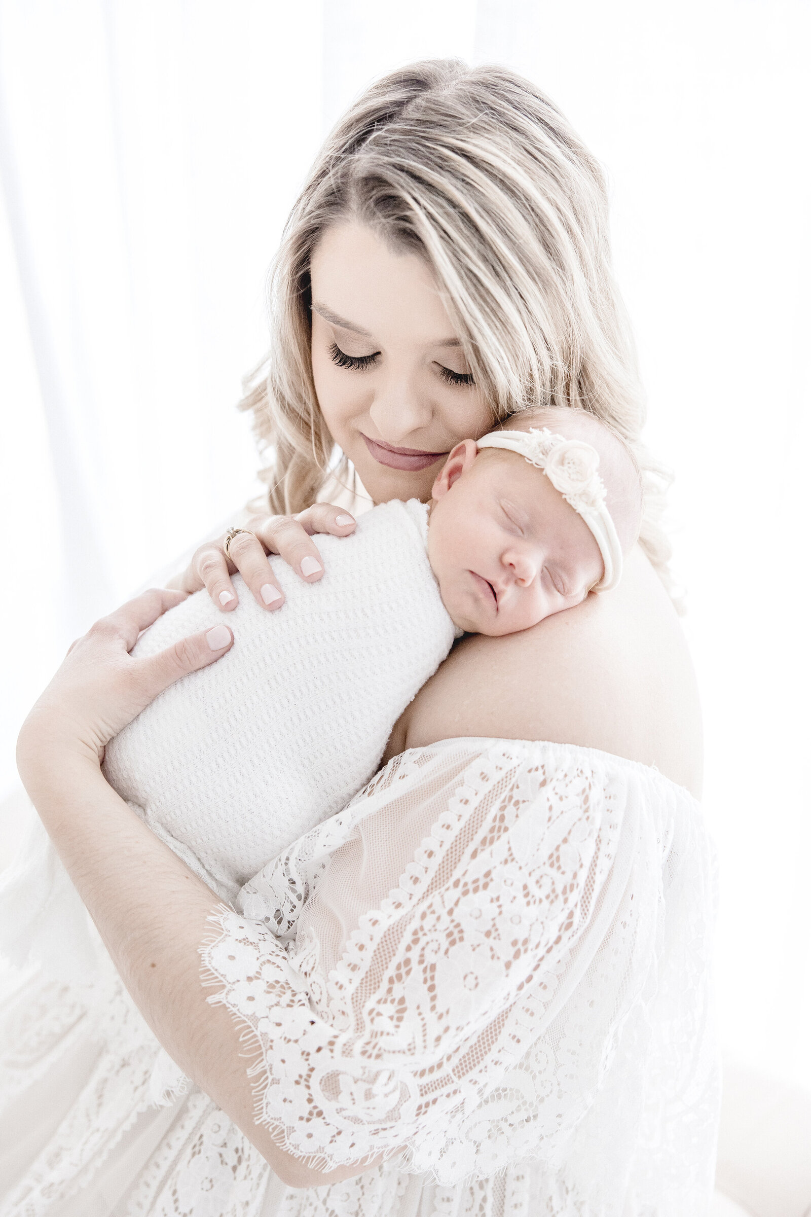 Woman in lace dress holdingsleeping newborn baby on sholder