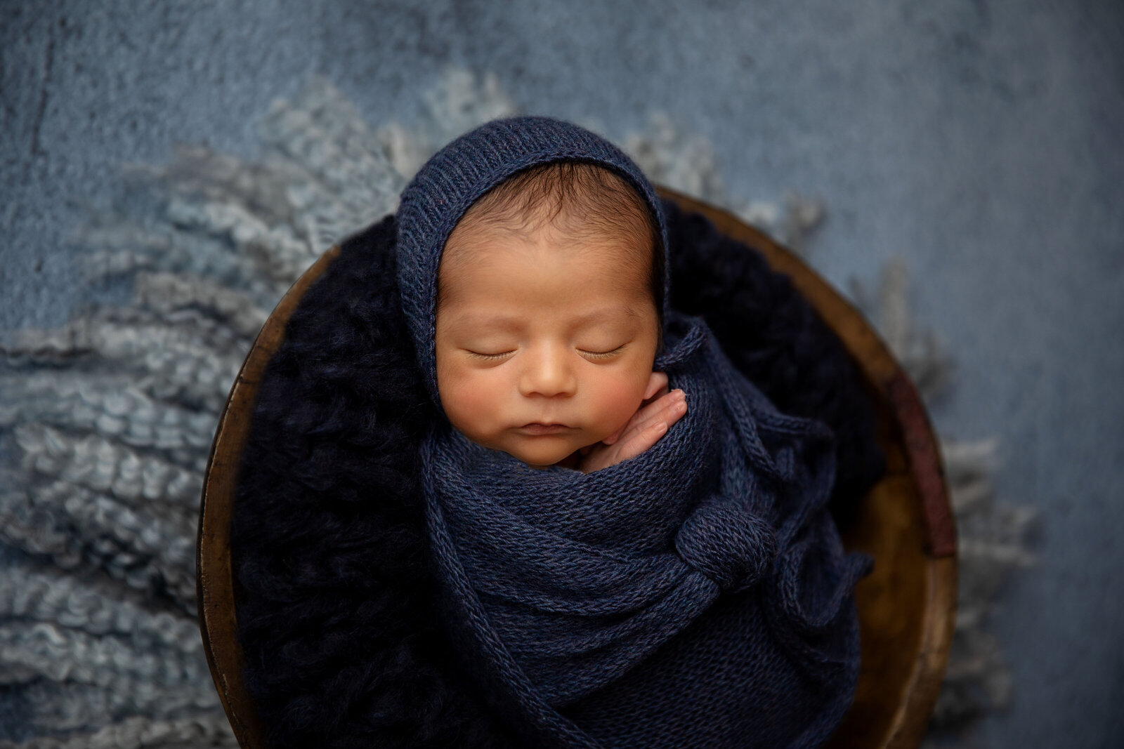 newborn baby boy in blue wrap inside brown bowl