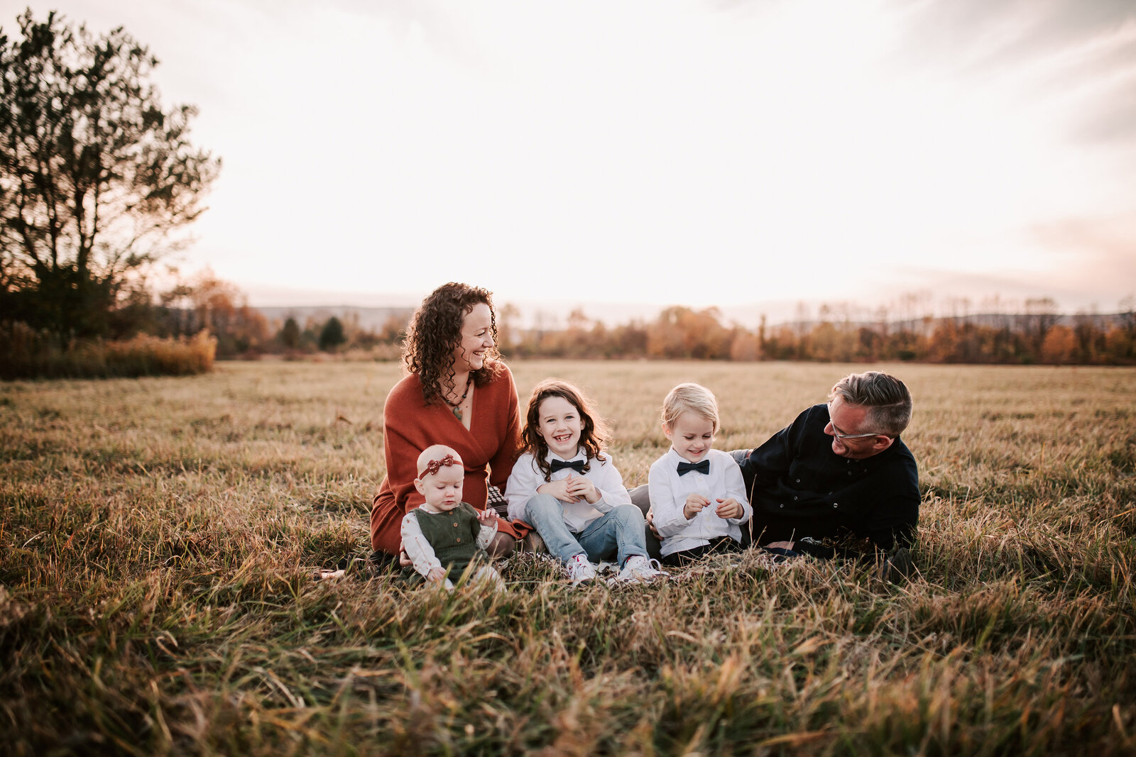 Family of five sitting in a grassy field at sunset laughing