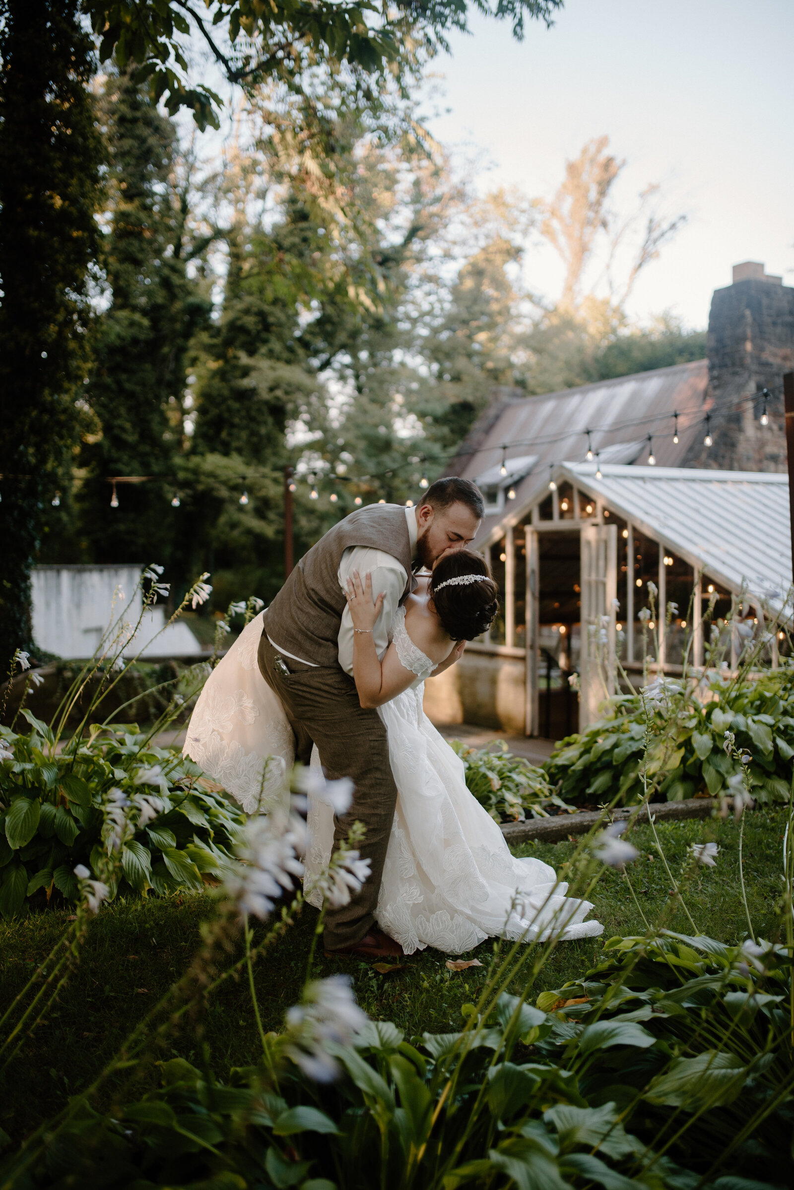 couple kissing in front of greenhouse surrounded by brush backwards dip Historic Shady Lane wedding