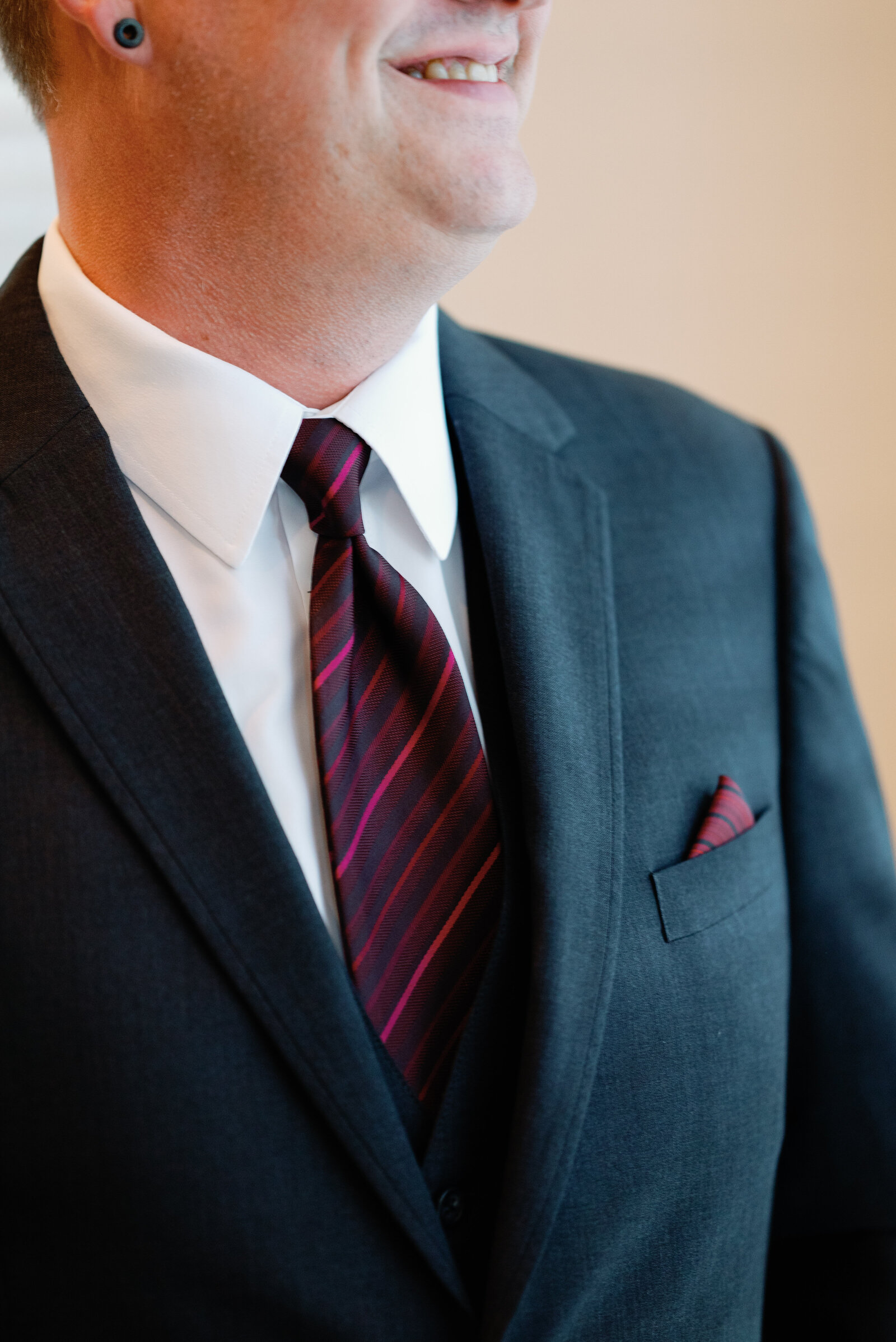 detail of grooms tie and usit jacket pocket square. Can also see his mouth smiling