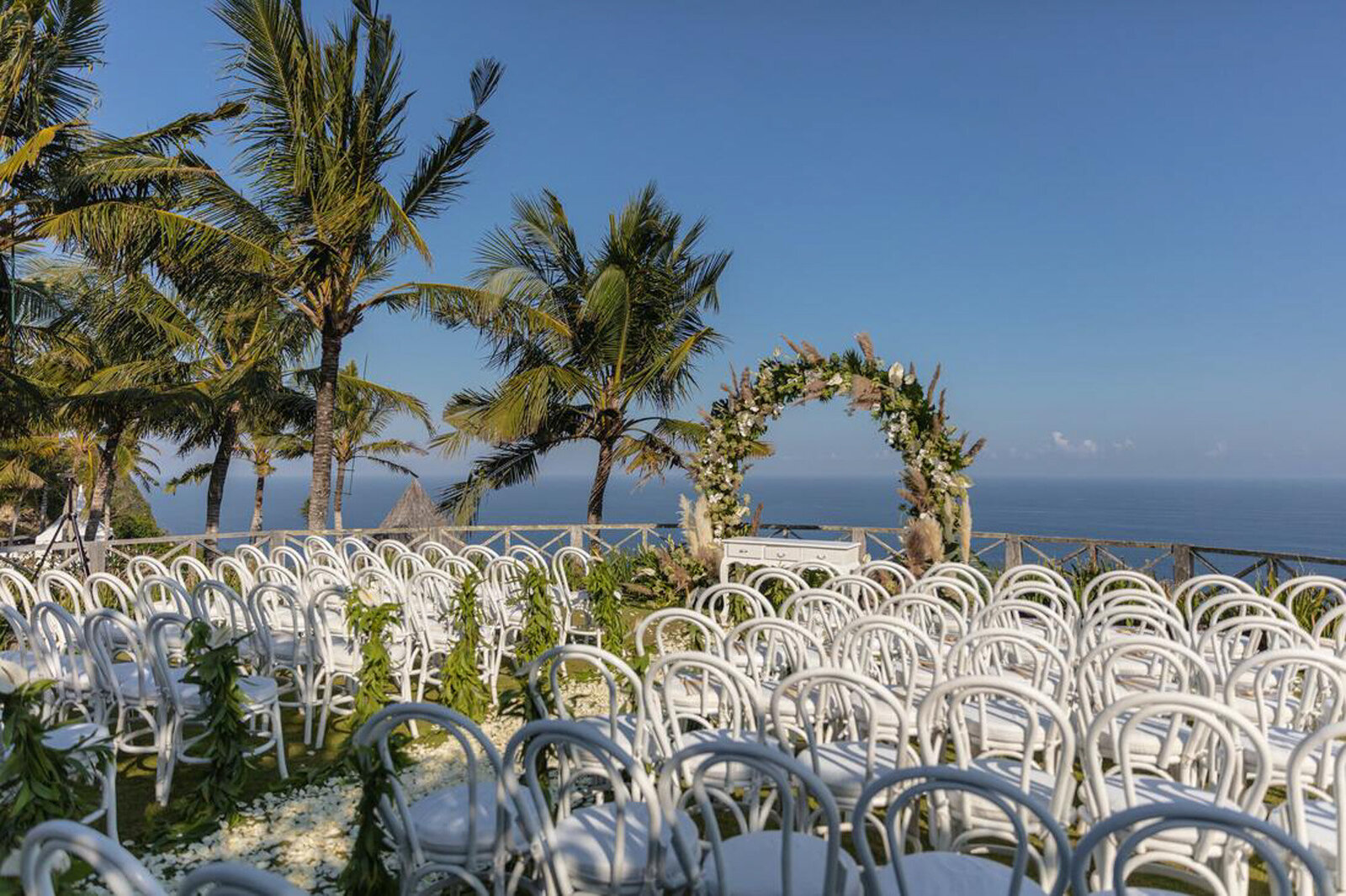 Beach wedding ceremony with white chairs and floral arch backdrop