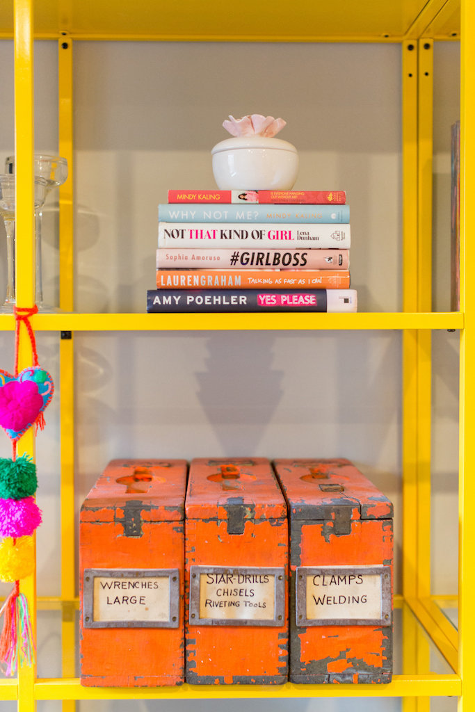 Yellow and glass shelve with orange canisters and a stack of books.
