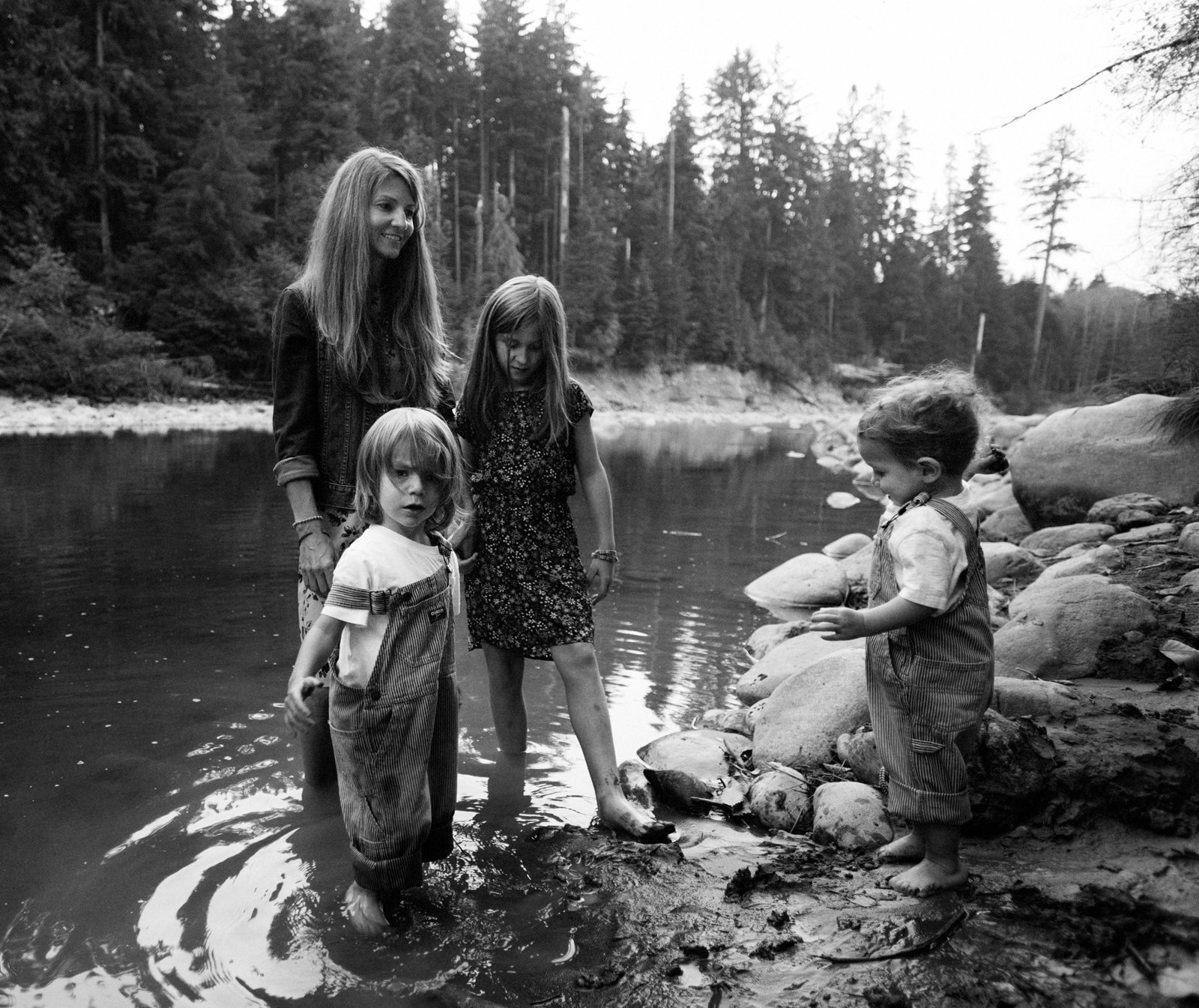 Black and white photo of mom and her three children wading in a river