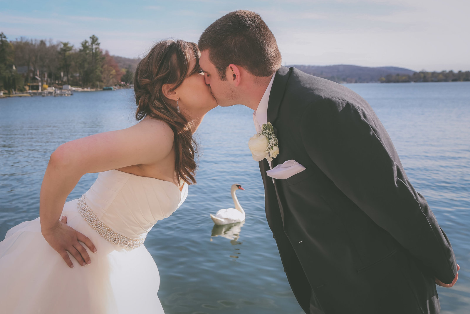A couple kisses by a California lake with swan in between them.