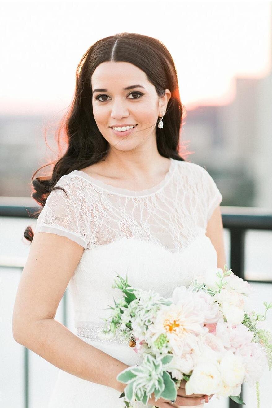 Dark-haired bride in wedding dress smiling at camera while holding a bouquet of flowers.
