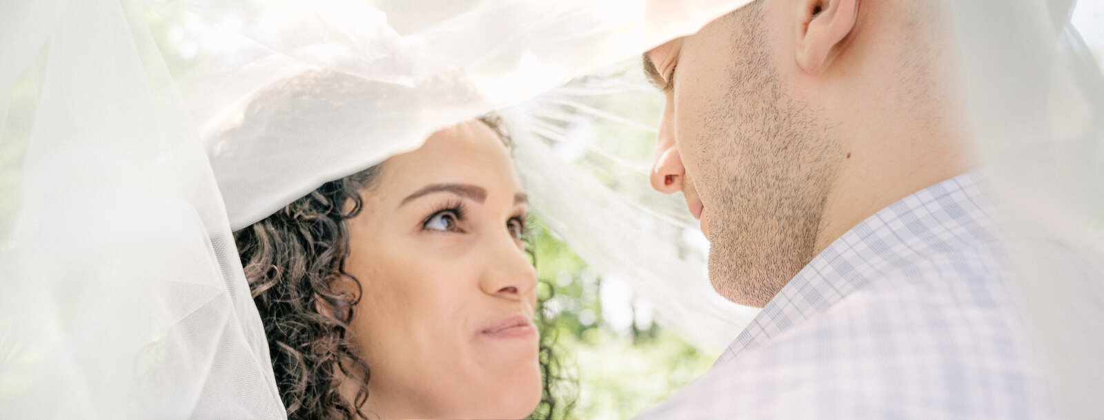 Naomi and John gaze into each other's eyes standing under a wedding veil