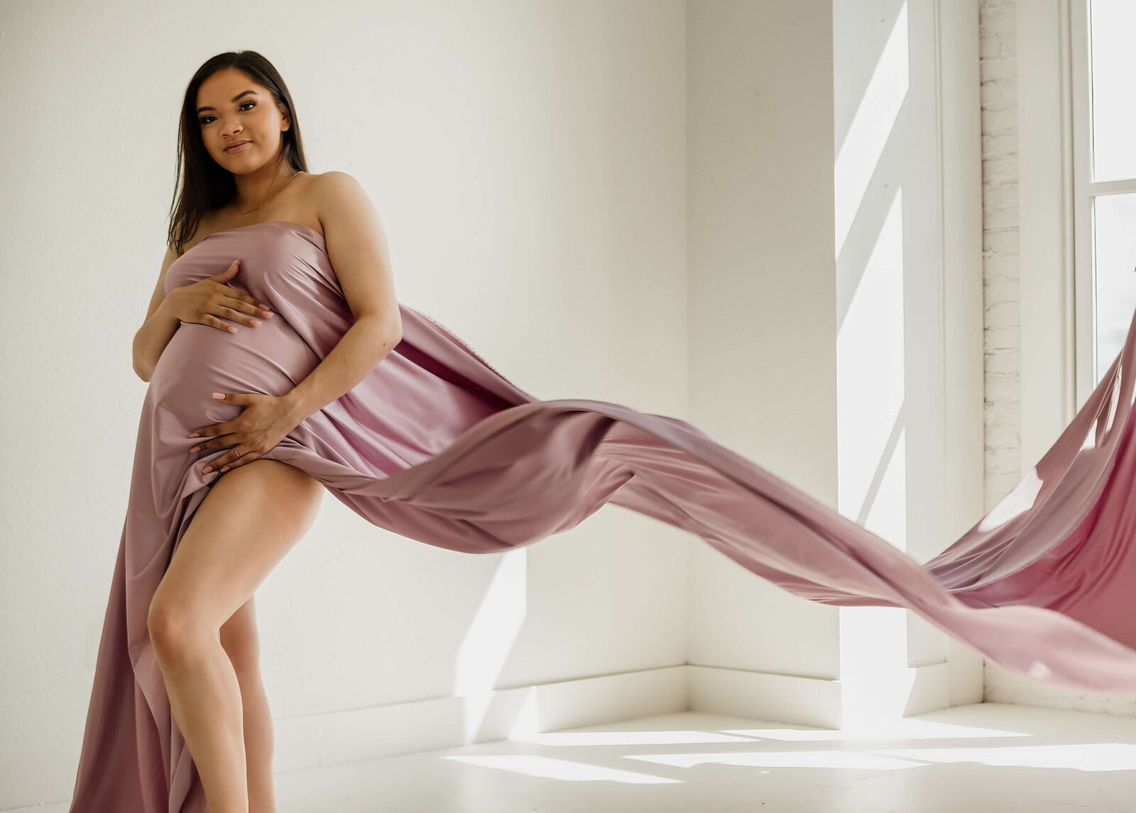 Pregnant woman draped in pink flowing fabric.