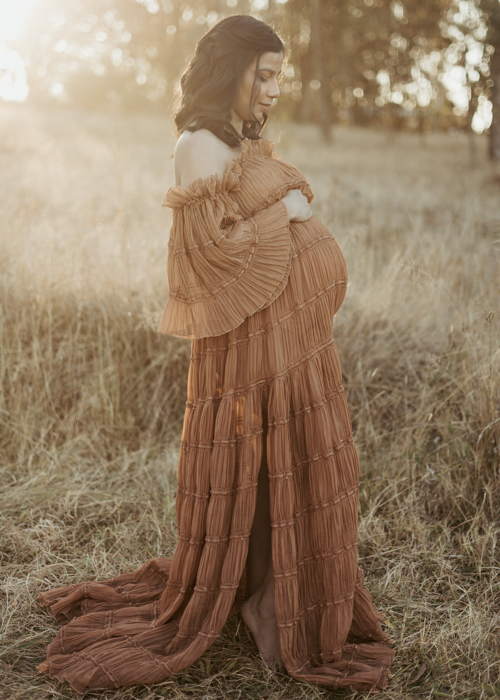 First time mum wearing a beautiful long brown dress in a grassy field at sunset