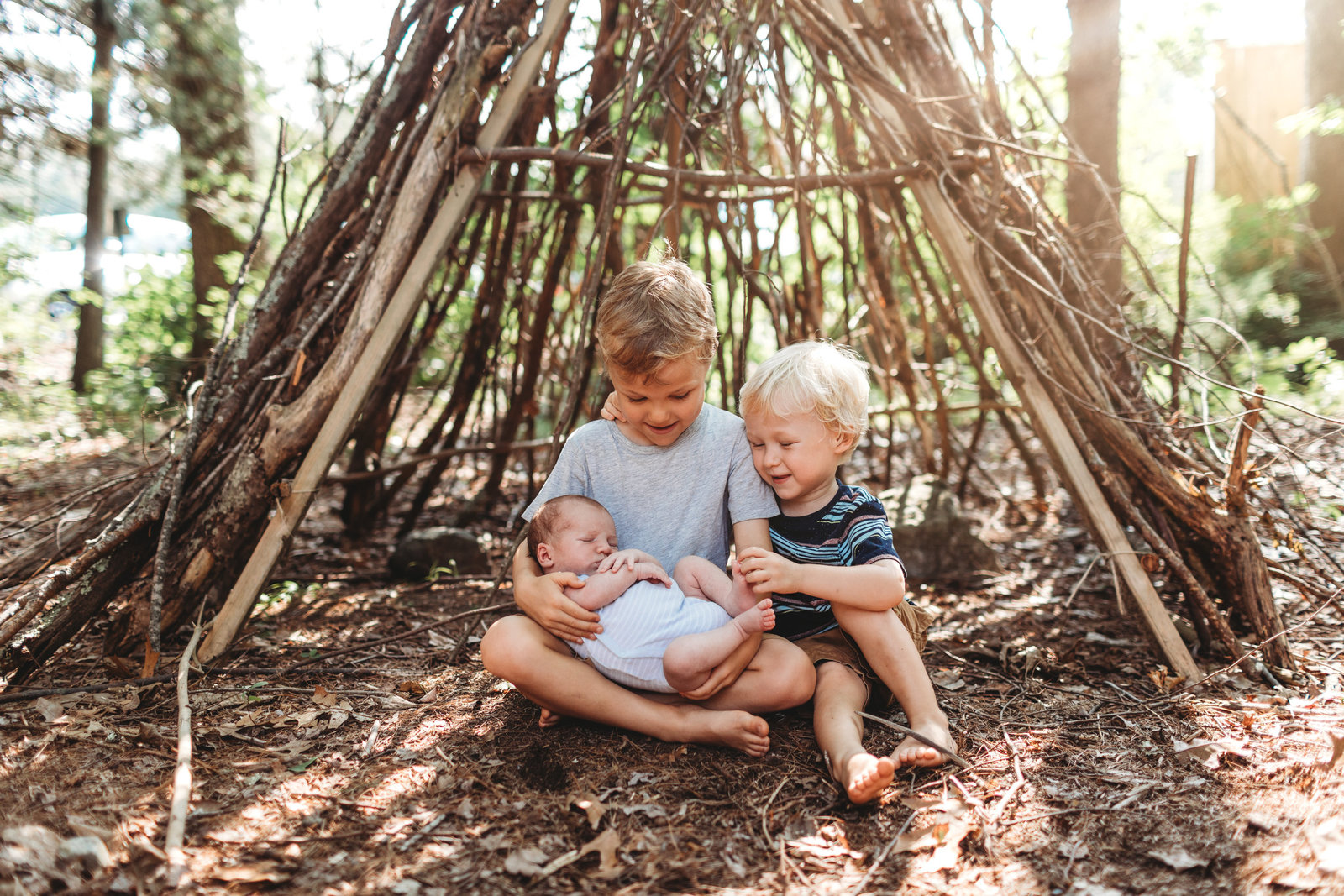 brothers hold new baby outdoors by stick teepee in lincoln ma