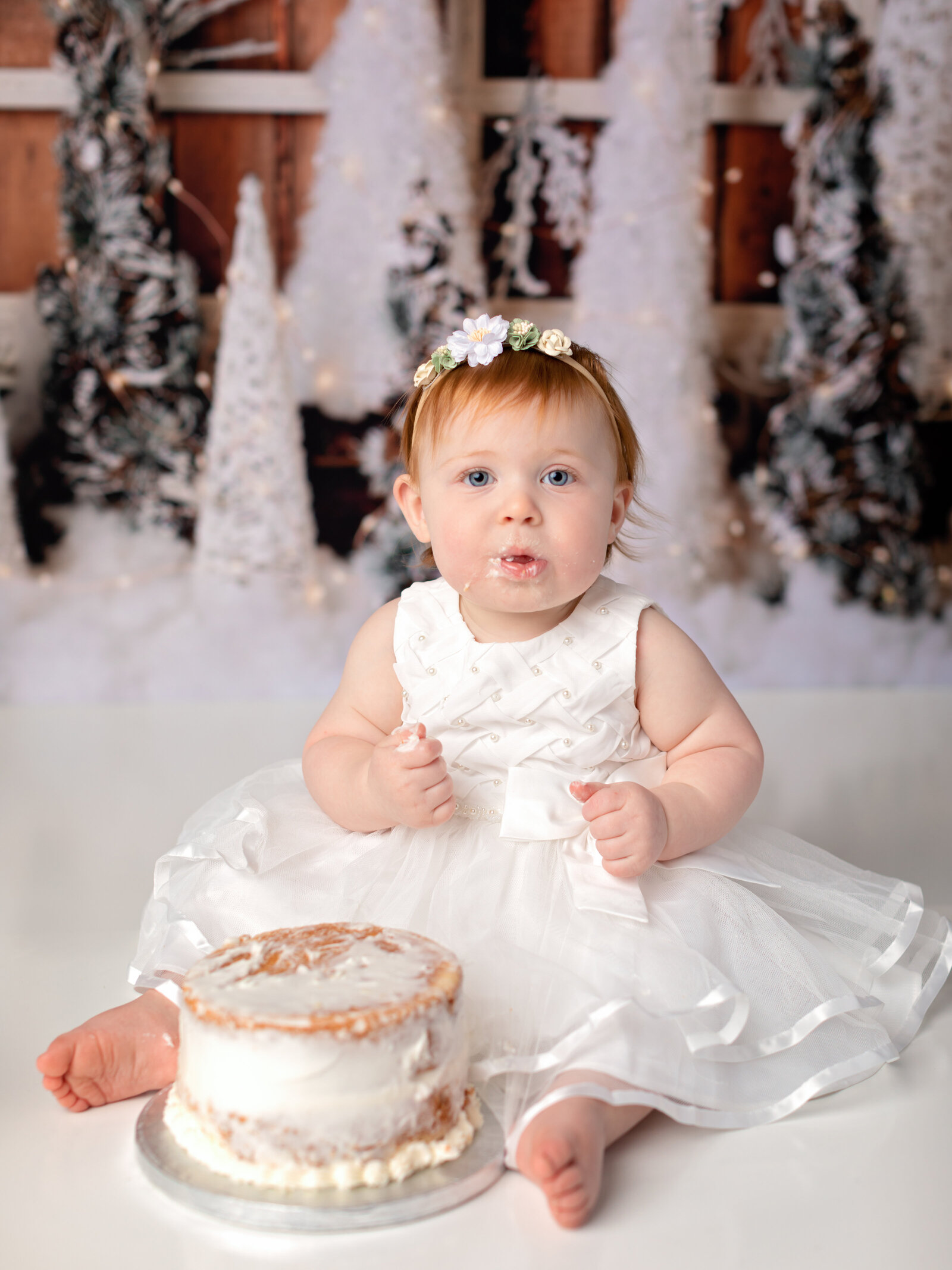 one year old girl in white dress smashing cake for photoshoot