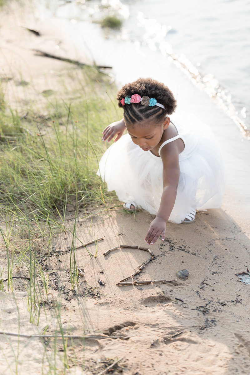 toddler traces the number two in the sand at birthday photo session