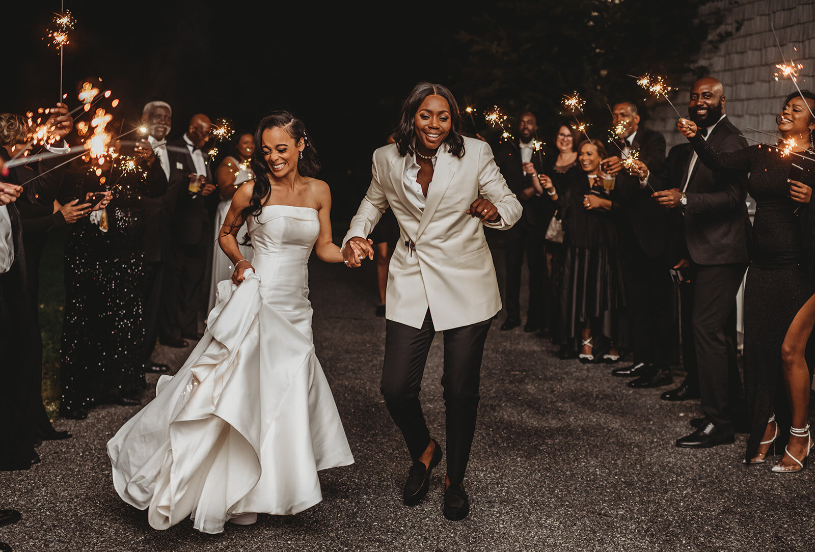 LGBTQ+ wedding with bride in a satin wedding dress and other bride in a dress suit with a white suit coat and black pants captured by Baltimore photographers
