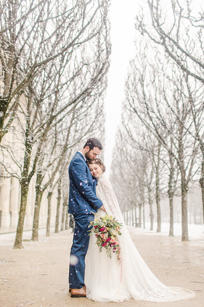 bride with her head on grooms chest and looking down at bouquet as it snows heavily in paris france