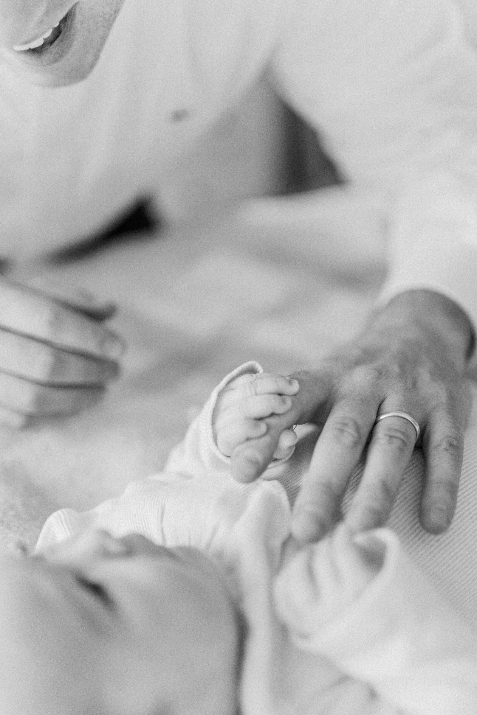 A close up black and white image of a father resting his hand on his baby girl's stomach while she grasps his finger during photo session with Boston newborn photographer Corinne Isabelle